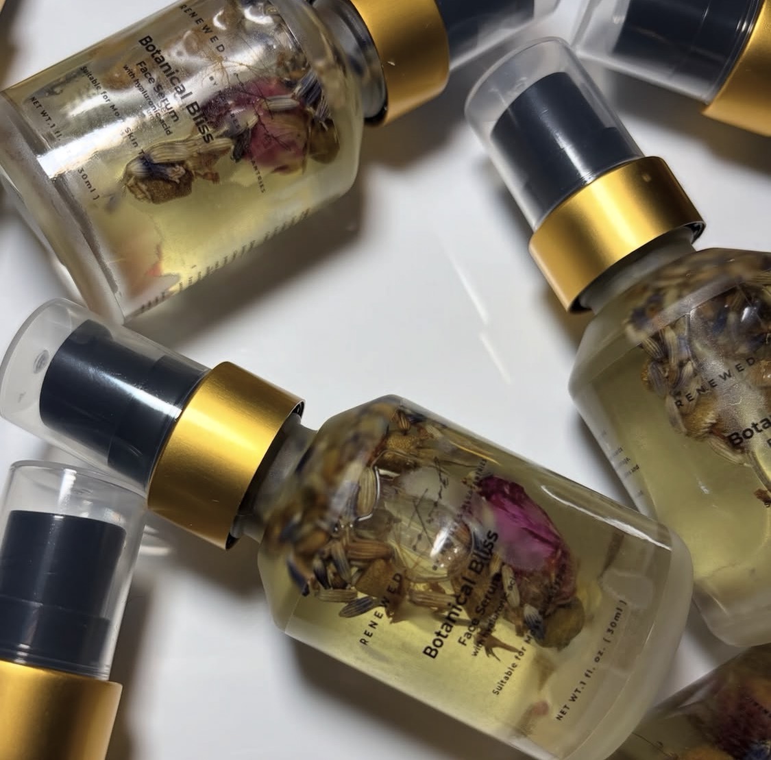 Botanical Bliss Face Serum product photo prompt: a refined glass dropper bottle labeled Botanical Bliss Face Serum on a neutral stone surface with soft linen and subtle botanical elements (fresh leaves, delicate herbs) arranged minimally; a few drops of serum visible on a glass dish; clean, calm luxury skincare aesthetic; diffused light, low contrast, preserved highlights; ultra-realistic editorial product photography.