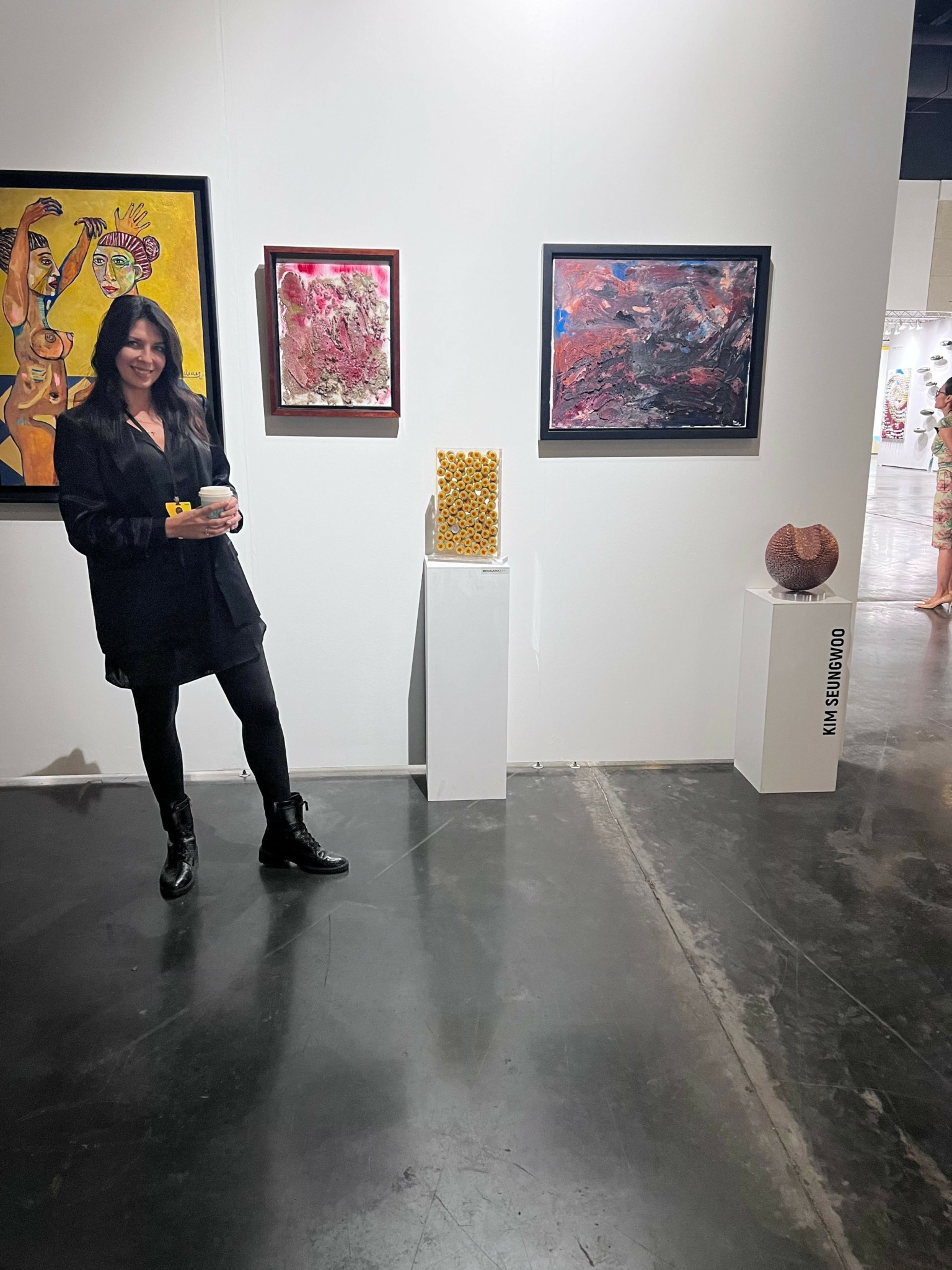 Woman standing in art gallery, three paintings on white wall, pedestal with yellow object, and sculpture on right.