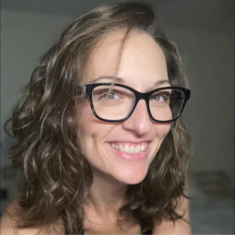 Woman with wavy hair and glasses smiling at camera.