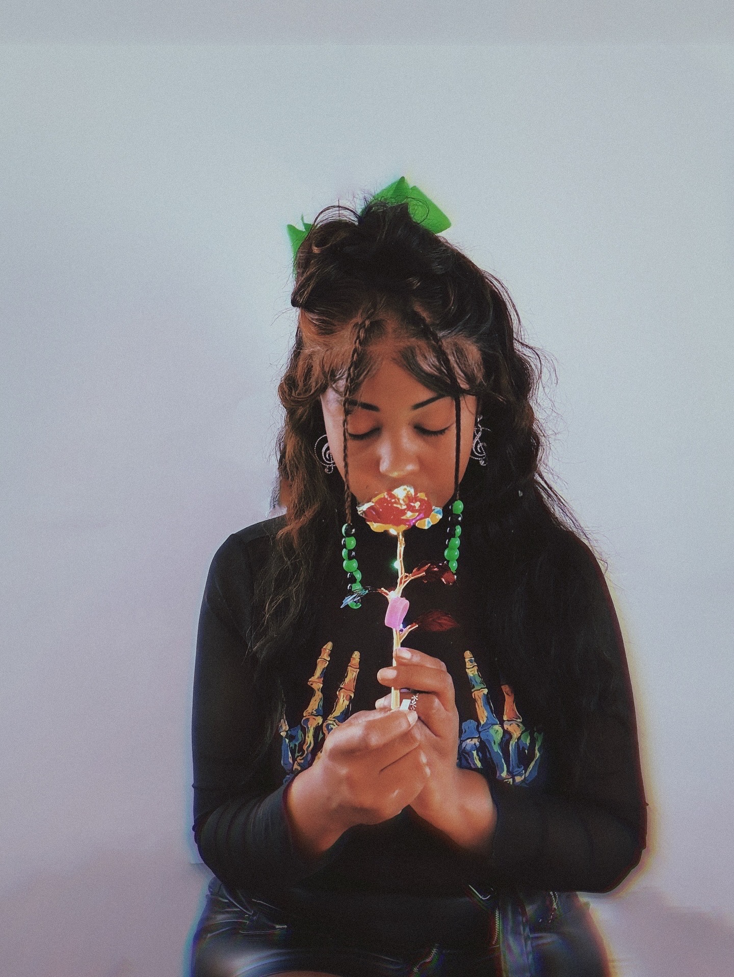 Girl with colorful hair accessories and beads, holding a pink object, looking down, against a plain background.