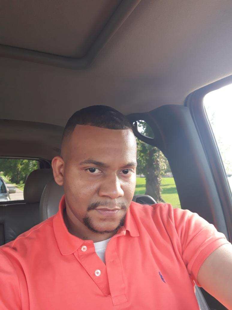Man with short hair wearing a red polo shirt sitting inside a vehicle, looking at the camera.