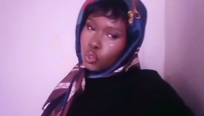 Person with a headscarf making a pouty face, looking at the camera, against a plain background.