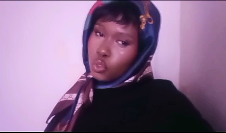 Young woman wearing a headscarf, making a pouty face, with a plain background.