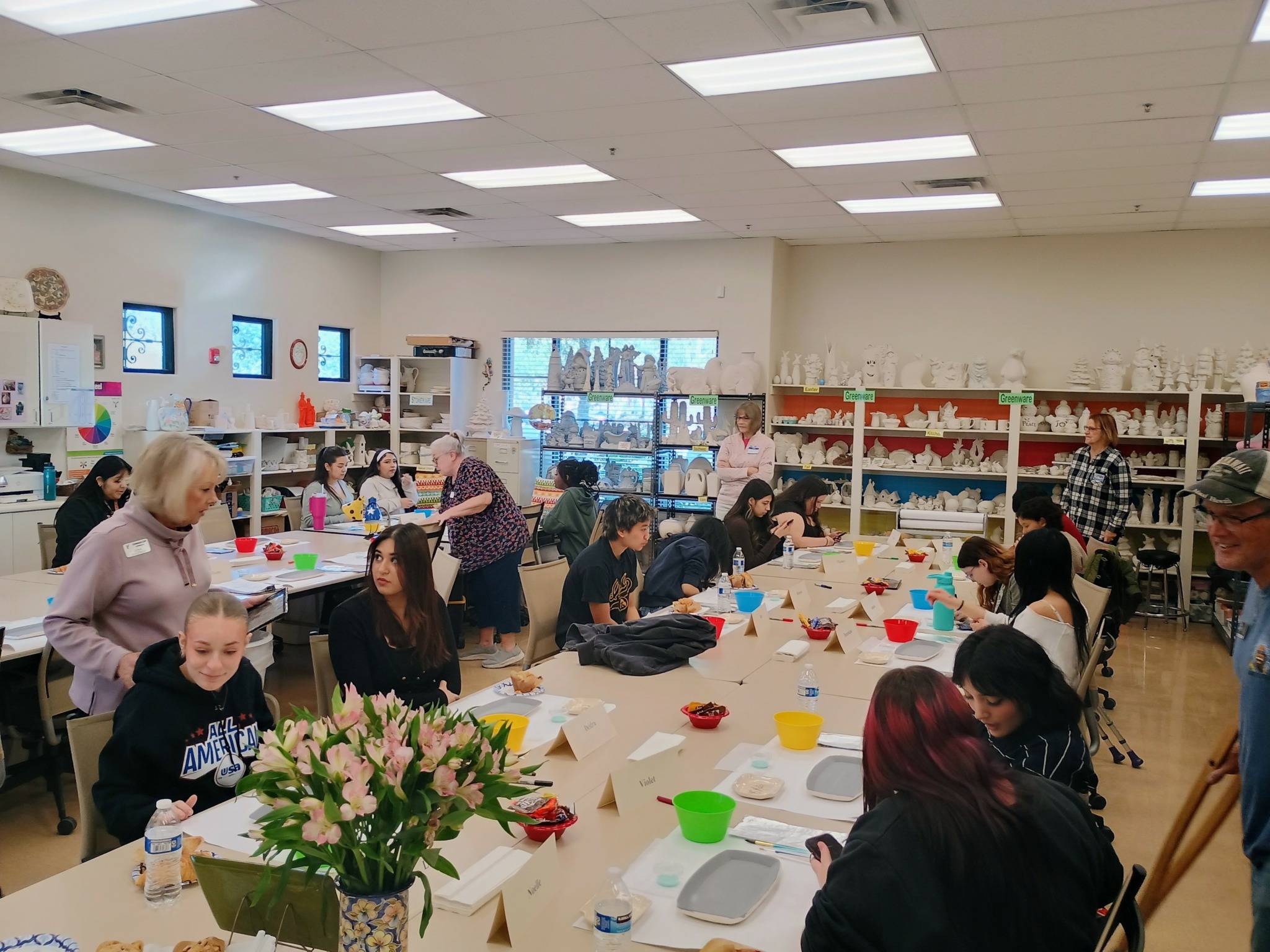 People gathered around tables in a craft room, working on projects with colorful materials and supplies.
