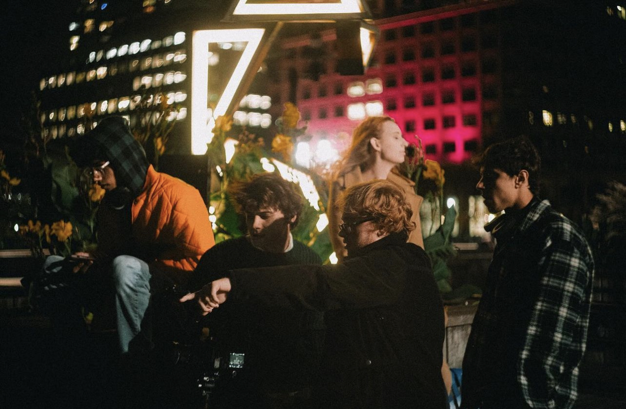 Group of five people sitting outdoors at night with city lights and buildings in background.
