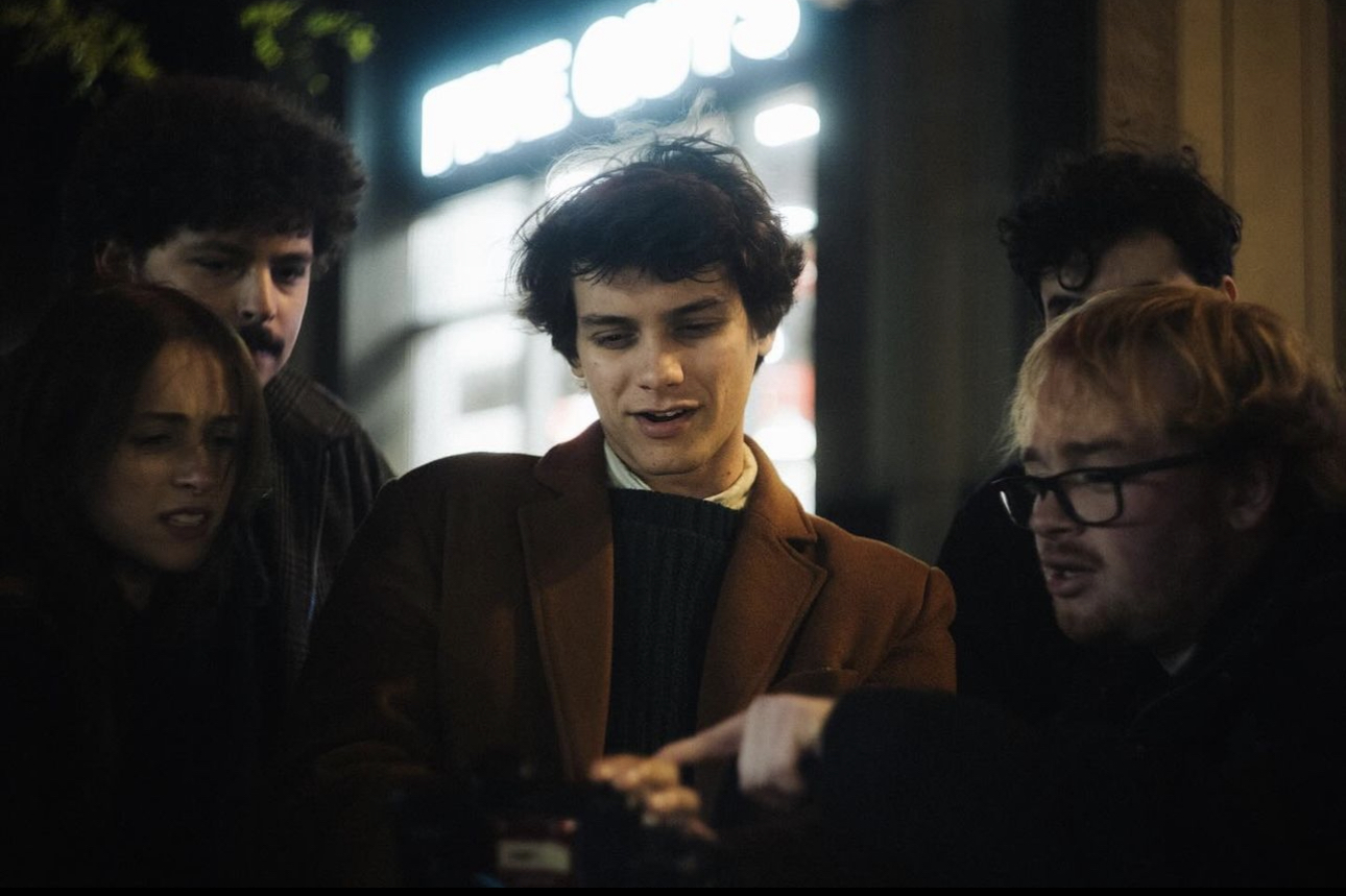 Group of five young people gathered around a table, looking at something together indoors.