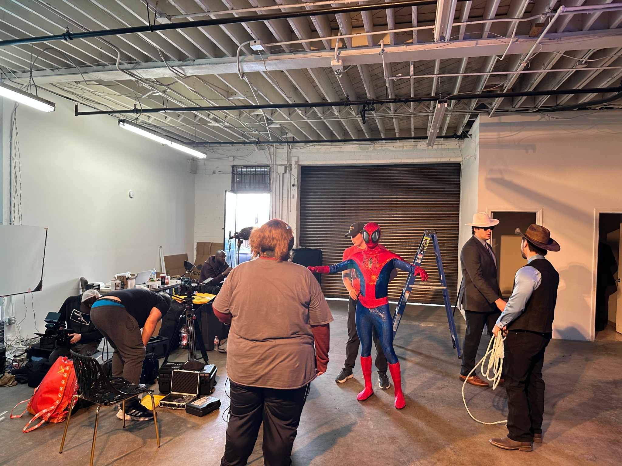 People in costumes and casual clothing gather in a warehouse with an open ceiling and a large closed door.
