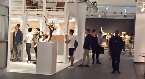 People browsing an art gallery with white display walls and sculptures, some looking at artwork and talking.