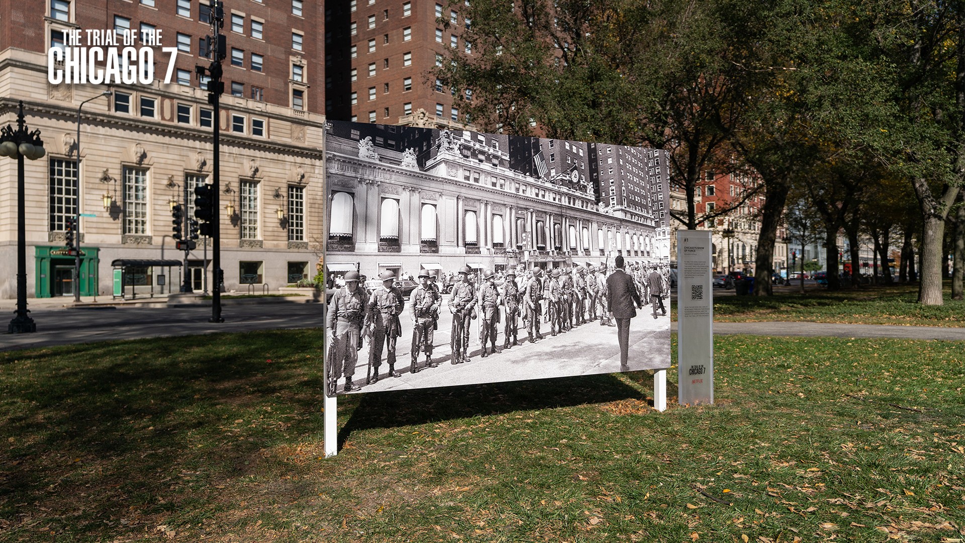 Historical black and white photo of soldiers and a person in front displayed outdoors on a panel.