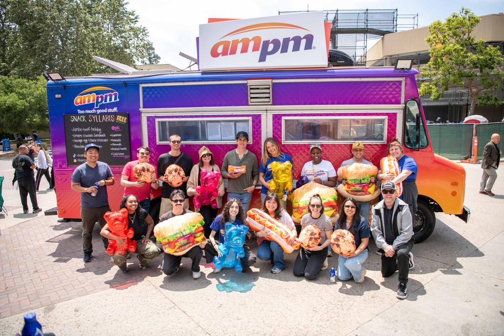 Group of people holding large bread loaves in front of a colorful food truck outdoors.