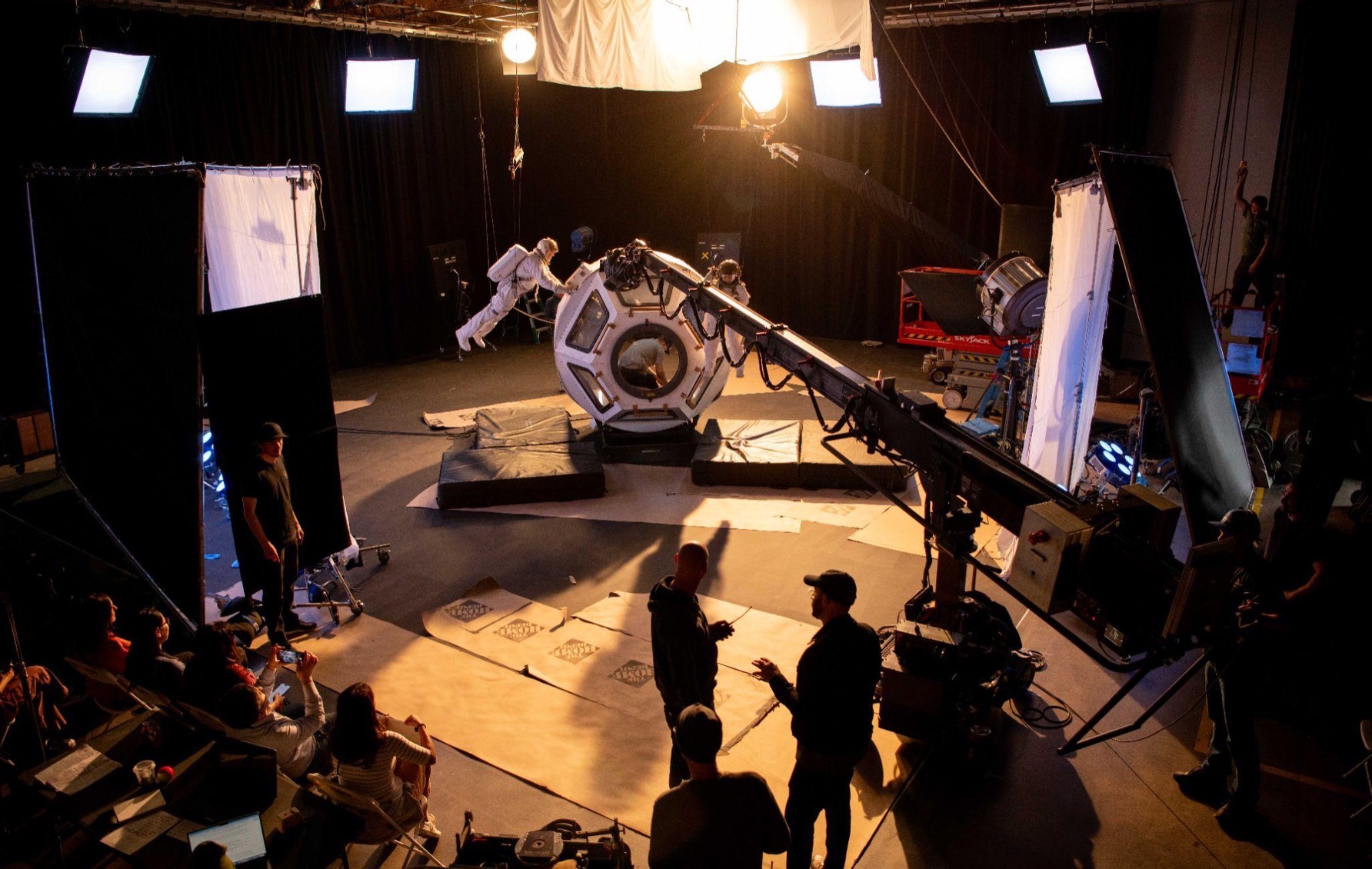 Studio with camera crane, large equipment, and crew preparing for filming or photography session.