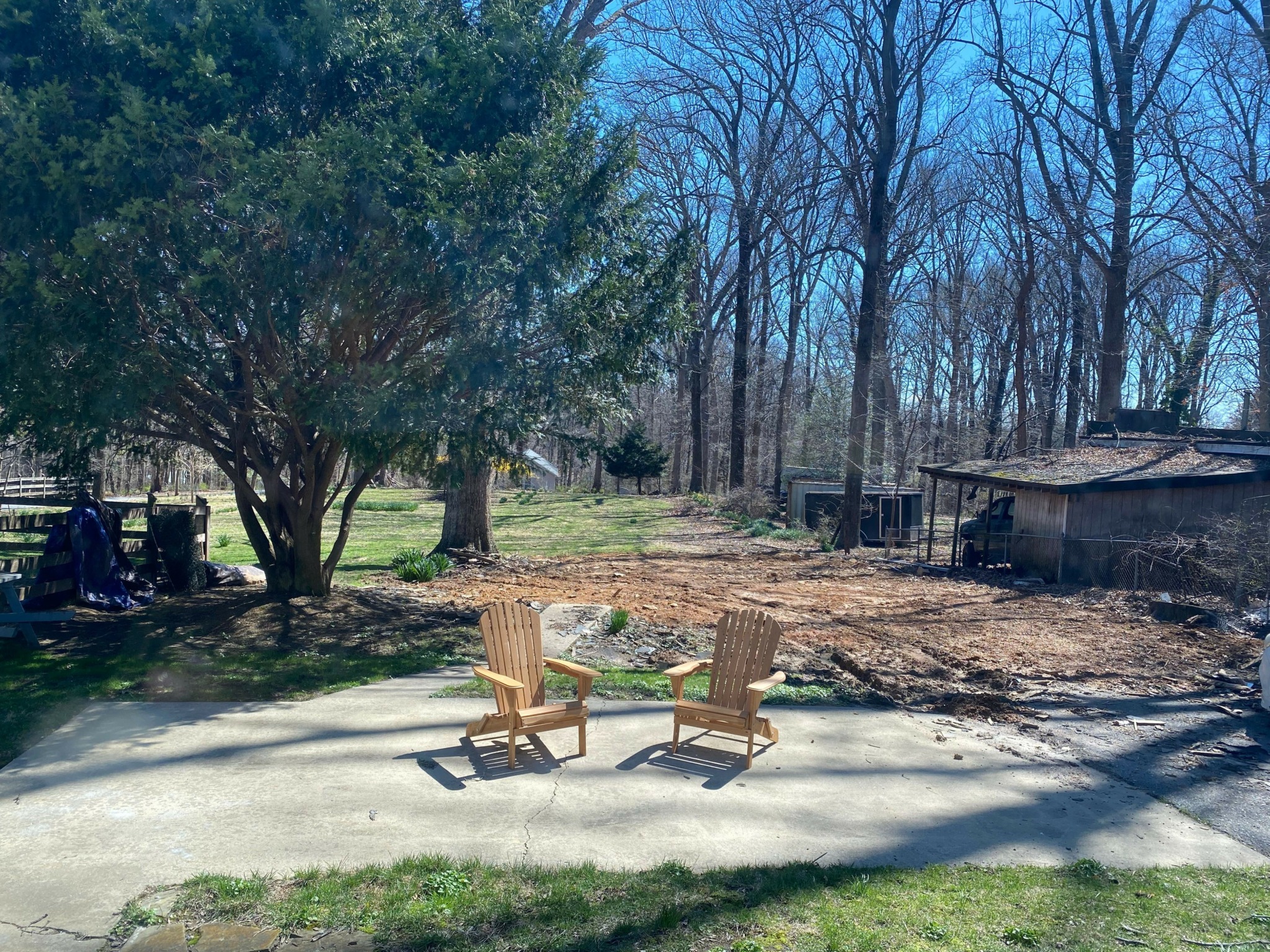 Two wooden chairs on a concrete patio with trees and a yard in the background.