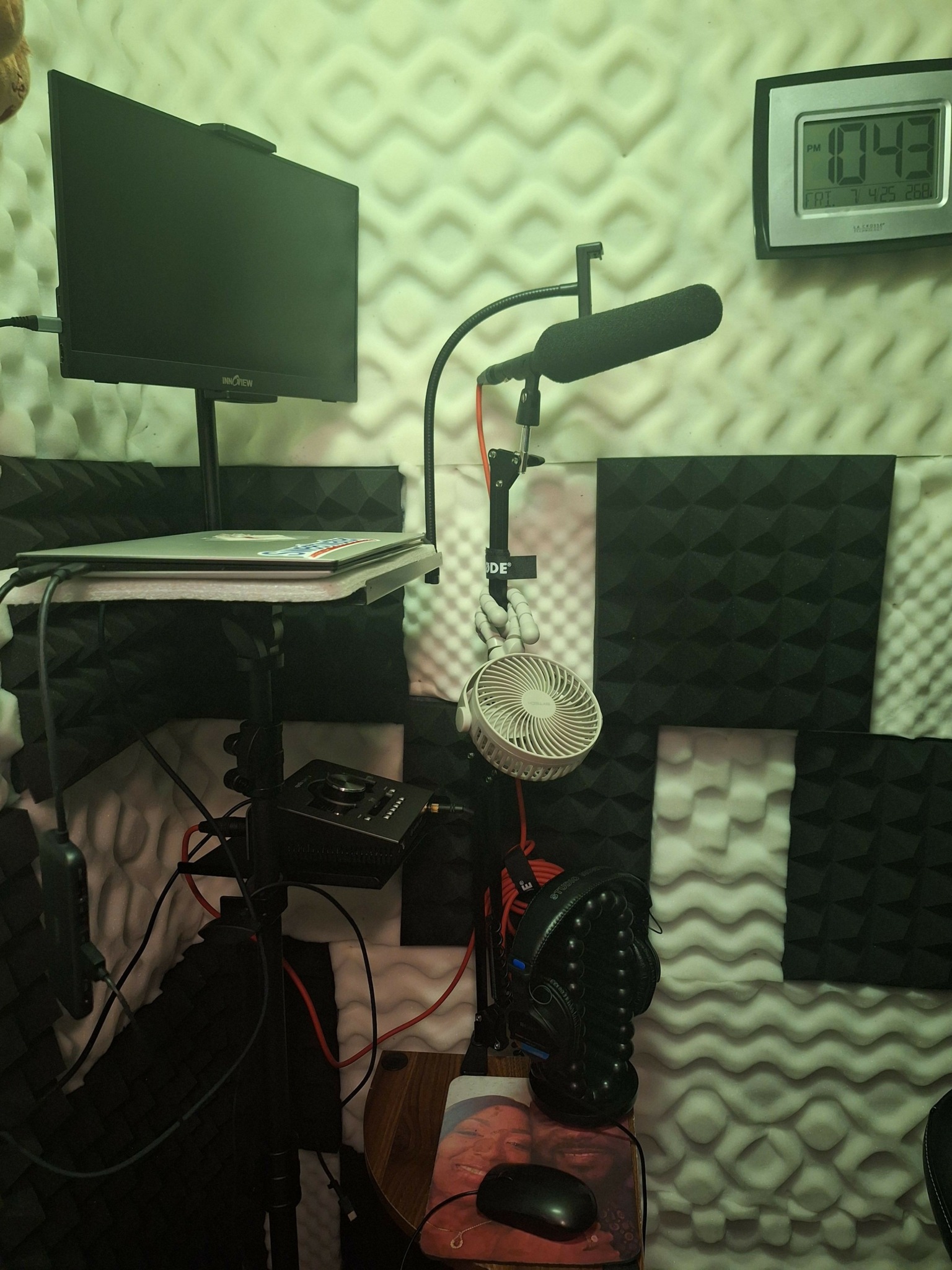 Recording studio with monitor, microphone, headphones, and soundproofing panels on wall.