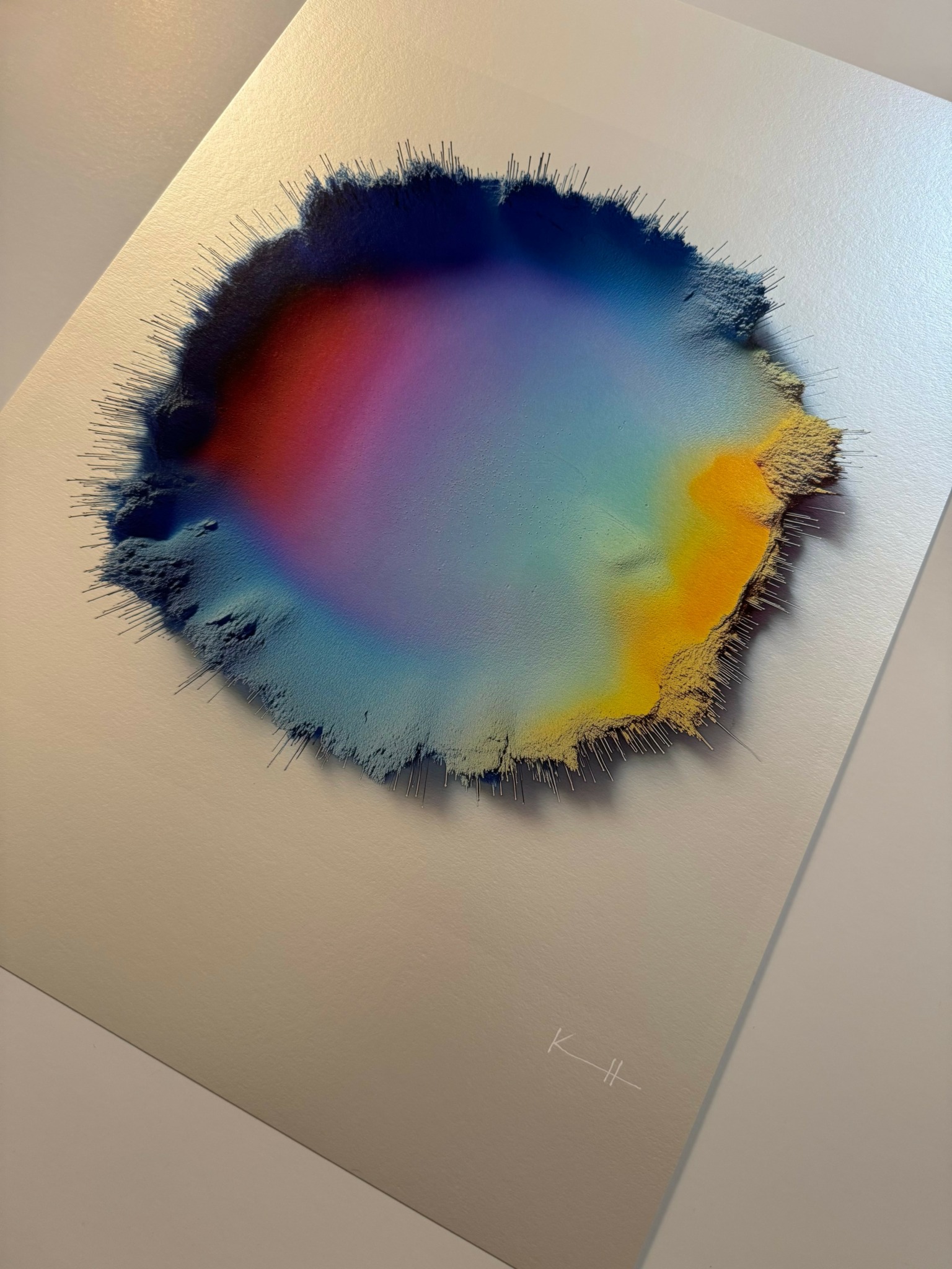 Abstract colorful ink or paint spread on paper with black edges, blending red, blue, yellow, and green hues.