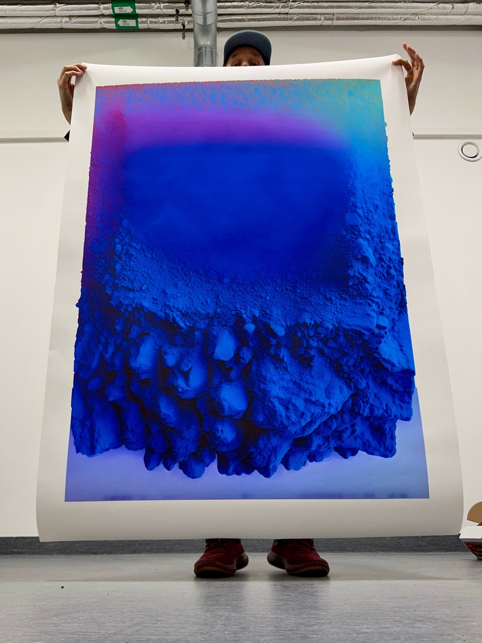 Person holding a large colorful abstract artwork with blue and purple hues, standing indoors.