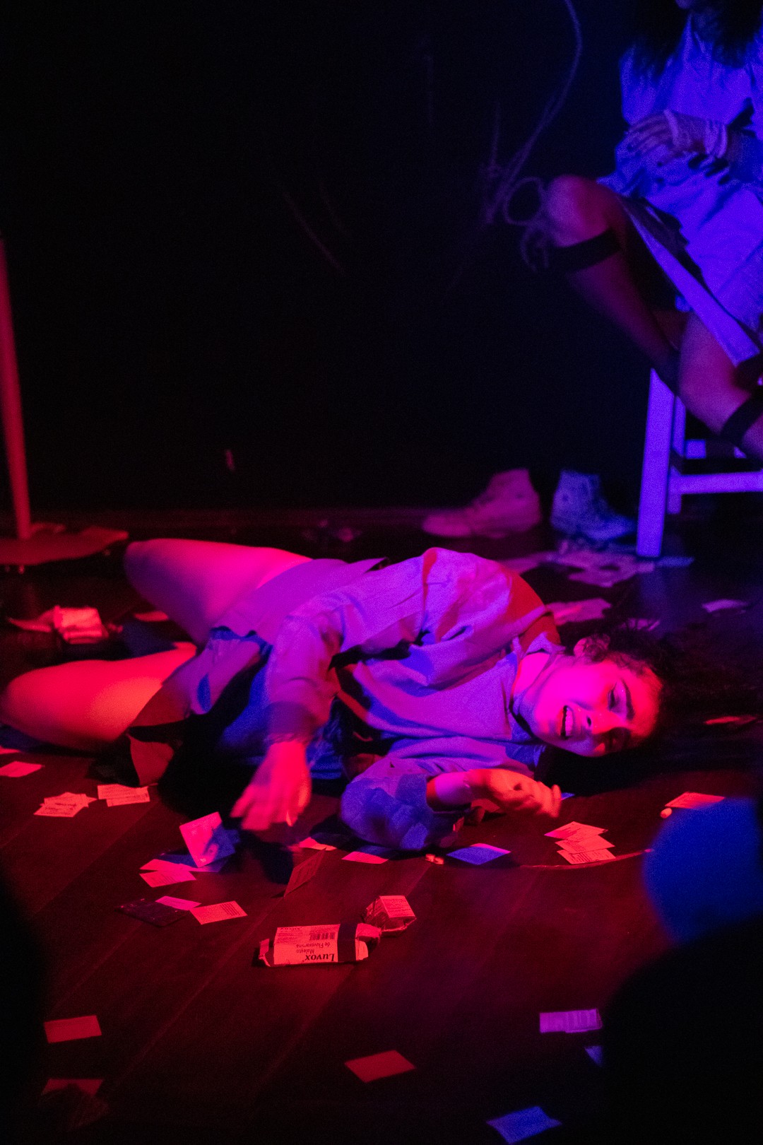 Person lying on the floor surrounded by scattered papers, illuminated by red and blue lighting.