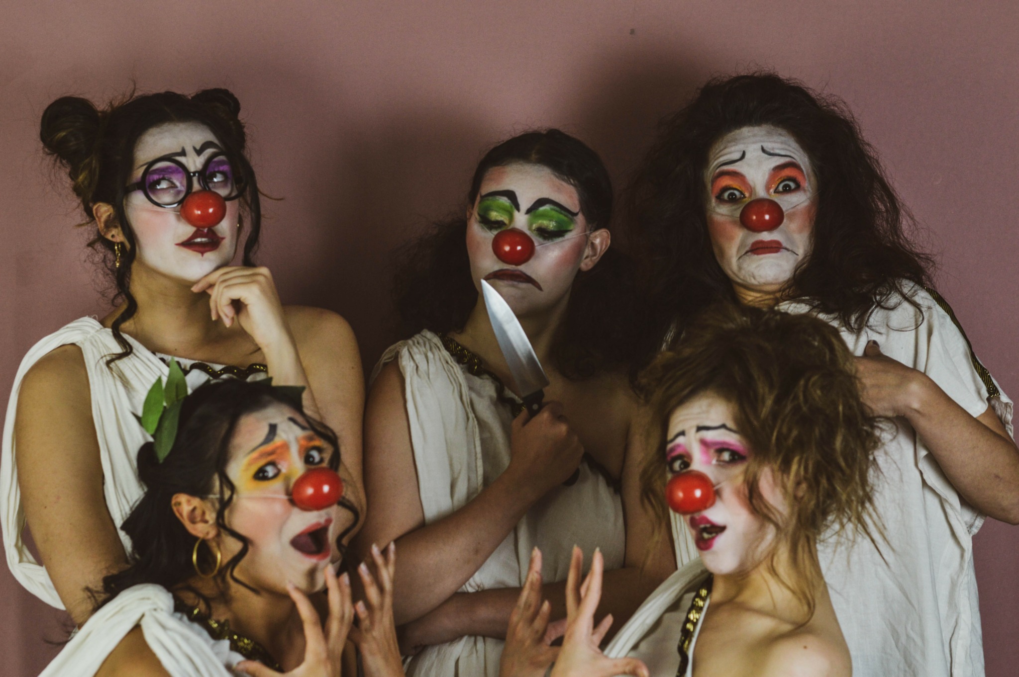 Five people dressed as clowns with painted faces and red noses, posing together against a plain background.
