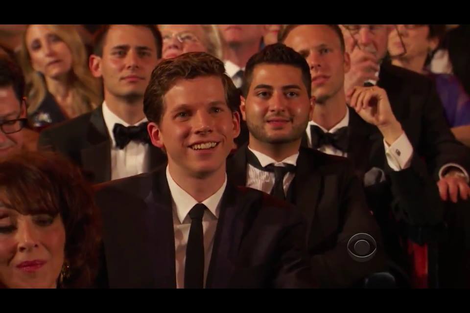 Group of people in formal attire attending an event, smiling and seated in rows.