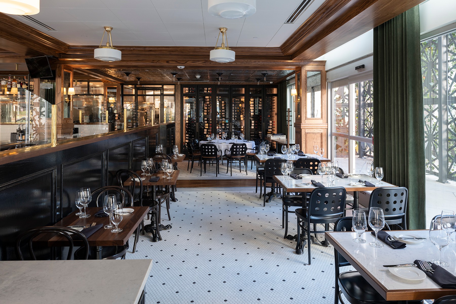 Elegant restaurant interior with wooden accents, black tables, and large windows with green curtains, set for dining.