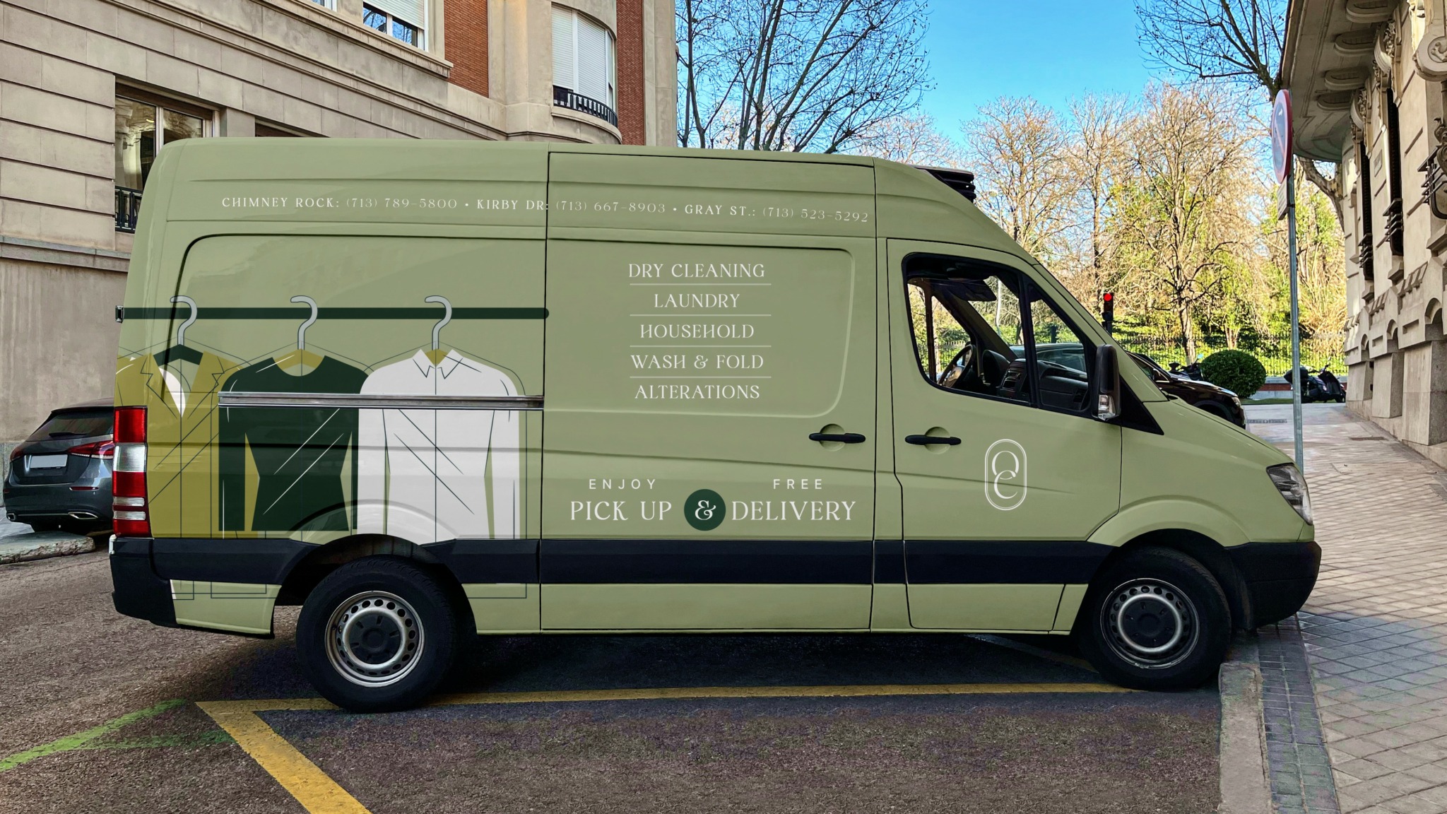 Green delivery van parked on street with text and graphics, trees and buildings in background.