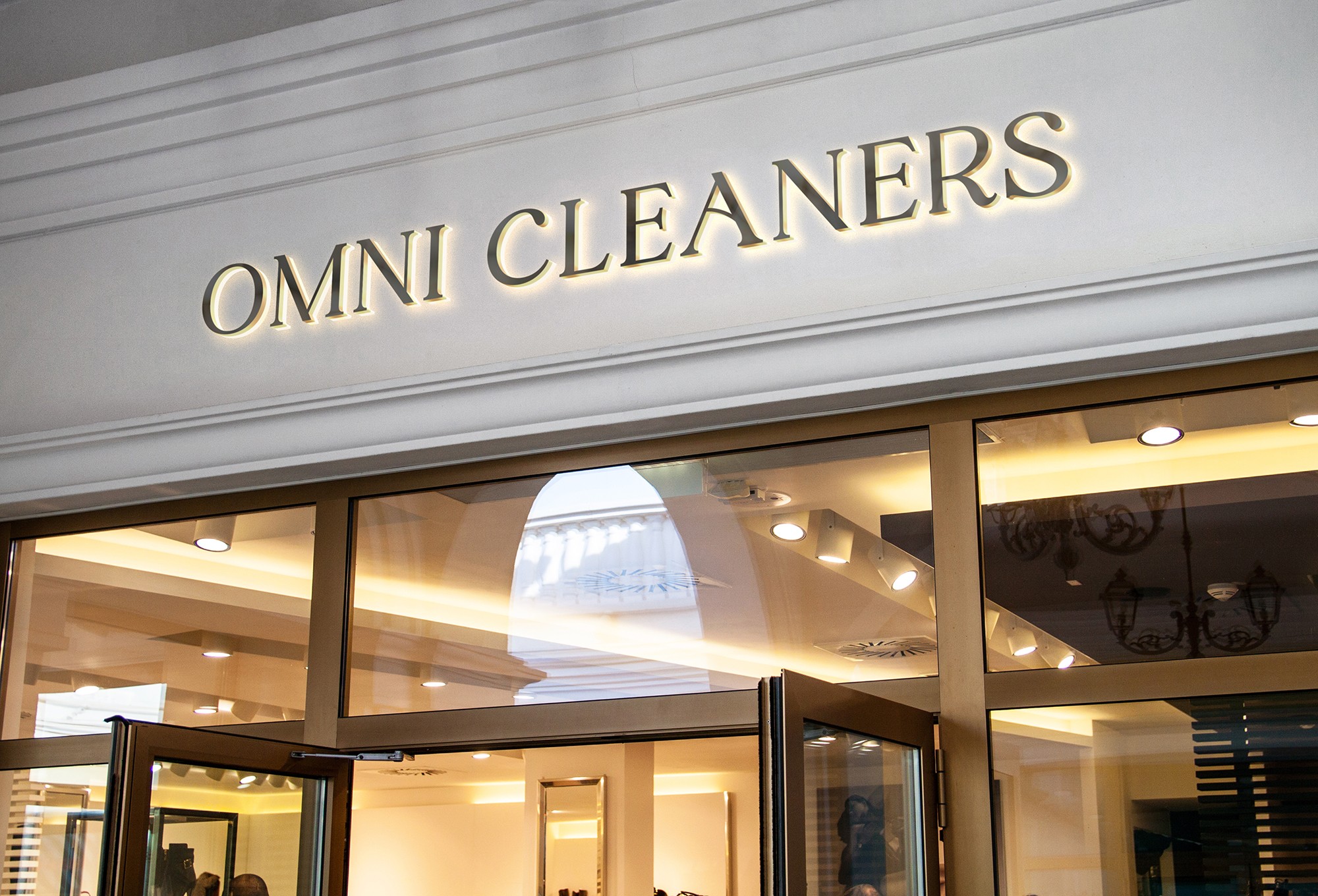 Storefront with sign reading 'OMNI CLEANERS' above entrance, glass doors, and interior lighting visible.