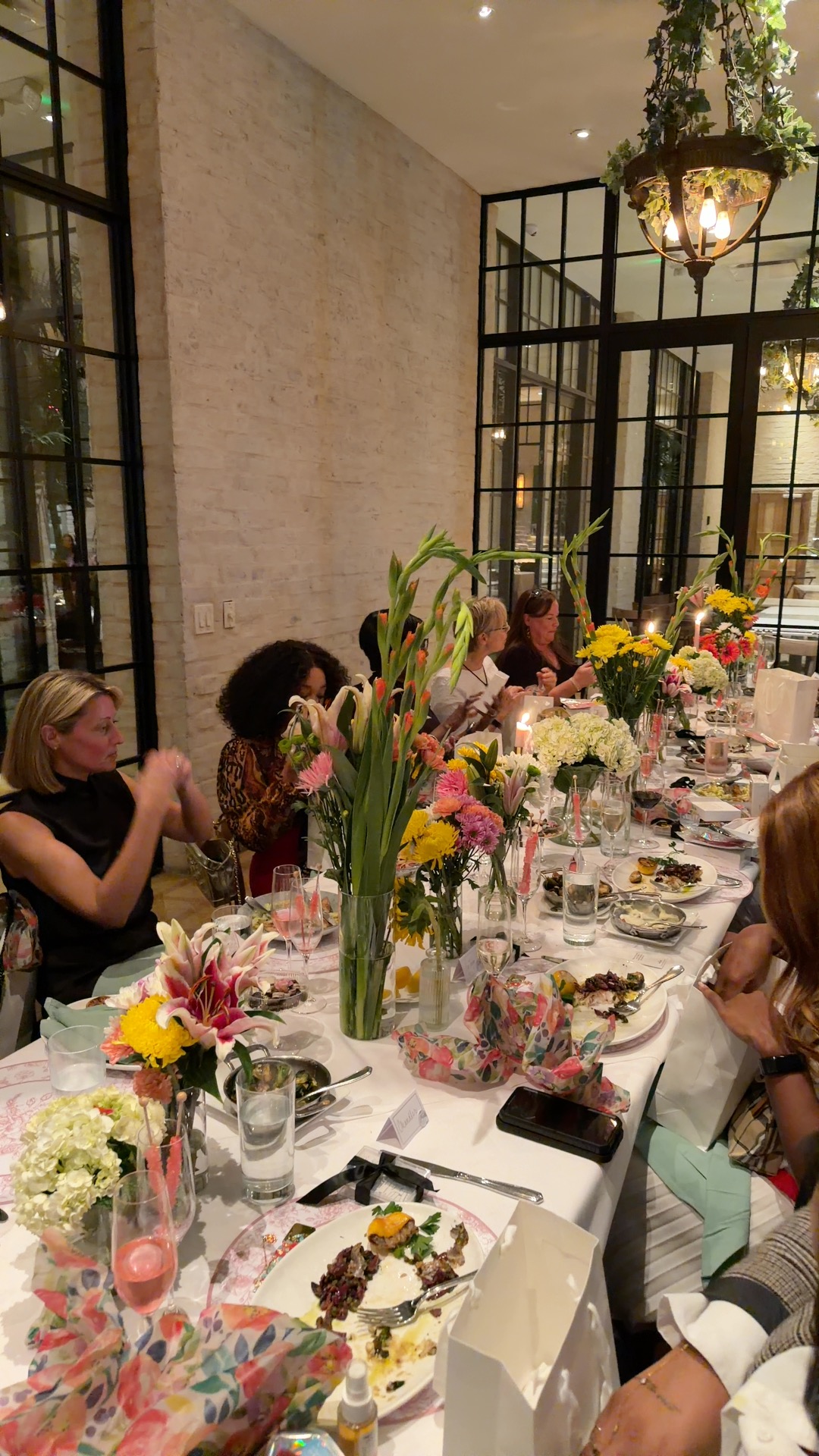 People seated at a long table with floral centerpieces and tableware in a bright, modern room.