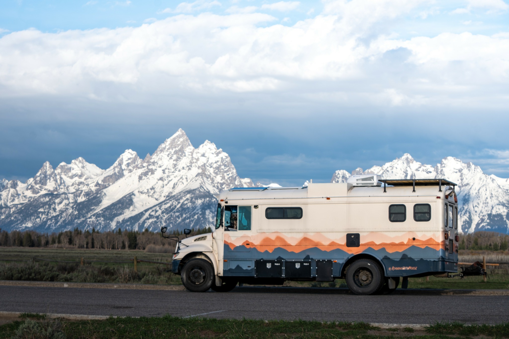 Camper van parked on a road with snow-capped mountains in the background under a cloudy sky.