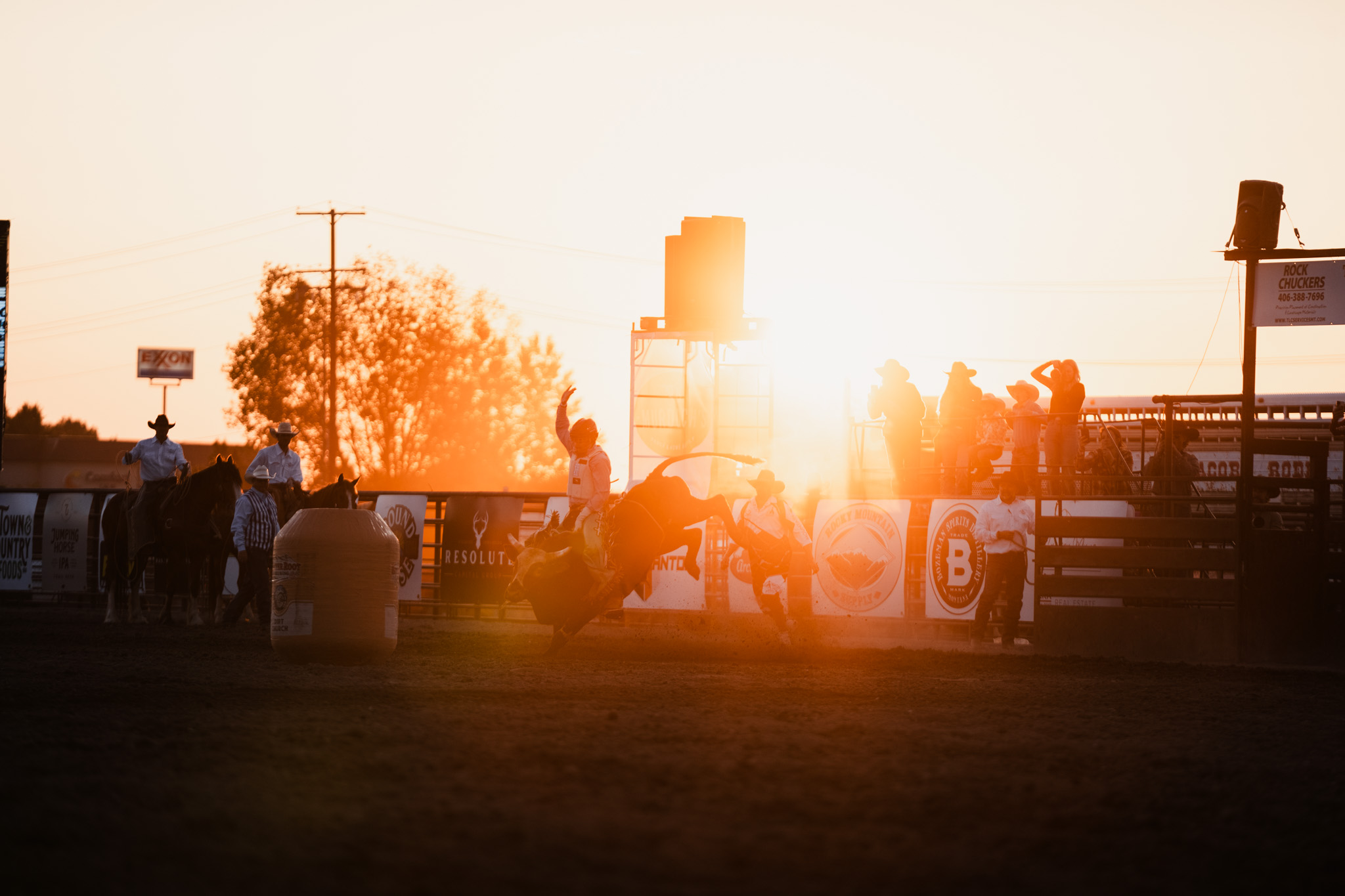 Silhouettes of people and a horse against a sunset at a rodeo or fairground.