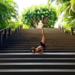 Person lying on stairs with one leg raised and foot pointing upward, surrounded by green trees and plants.