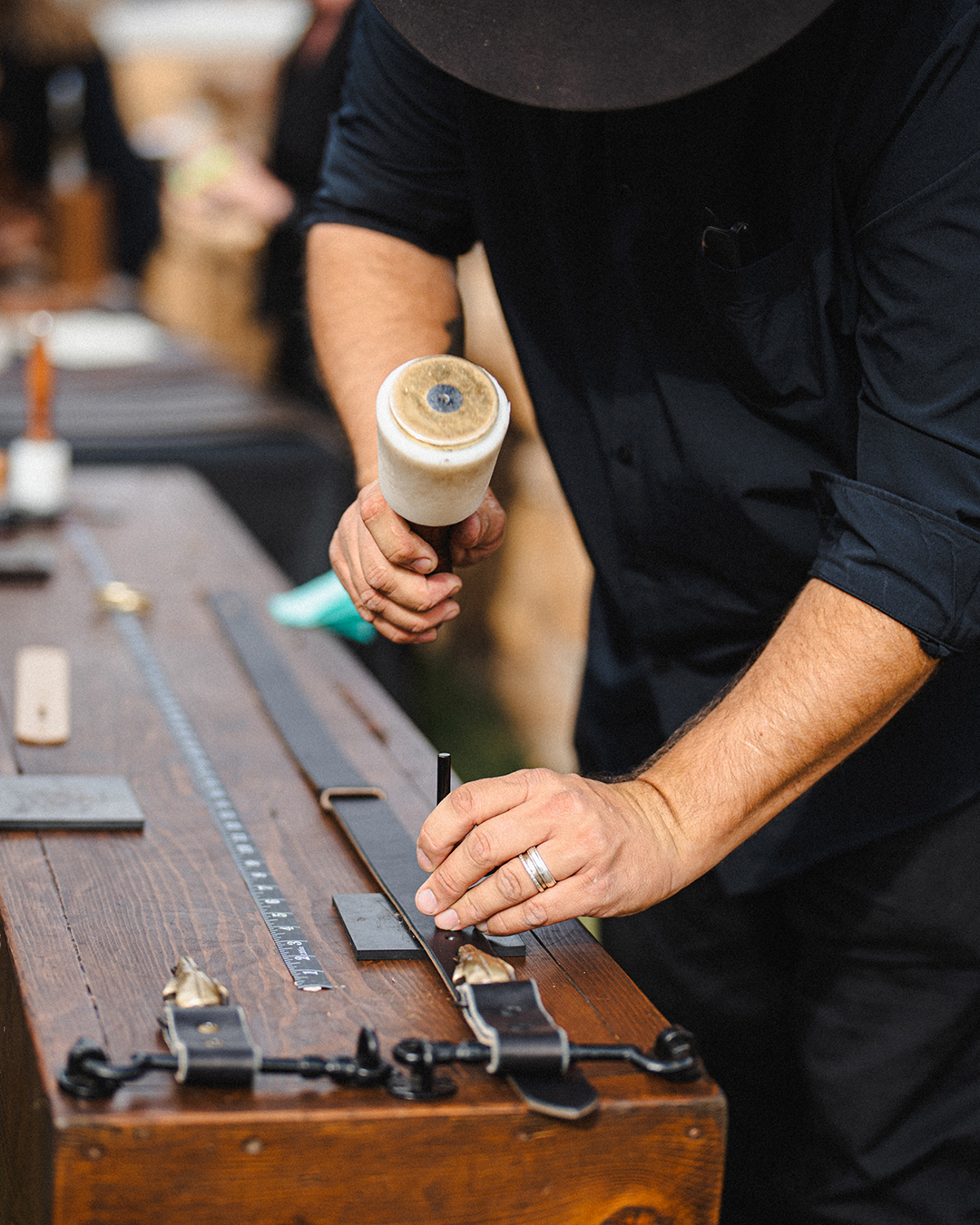 Person working with leather tools on a wooden workbench, wearing a dark shirt and a ring on their finger.