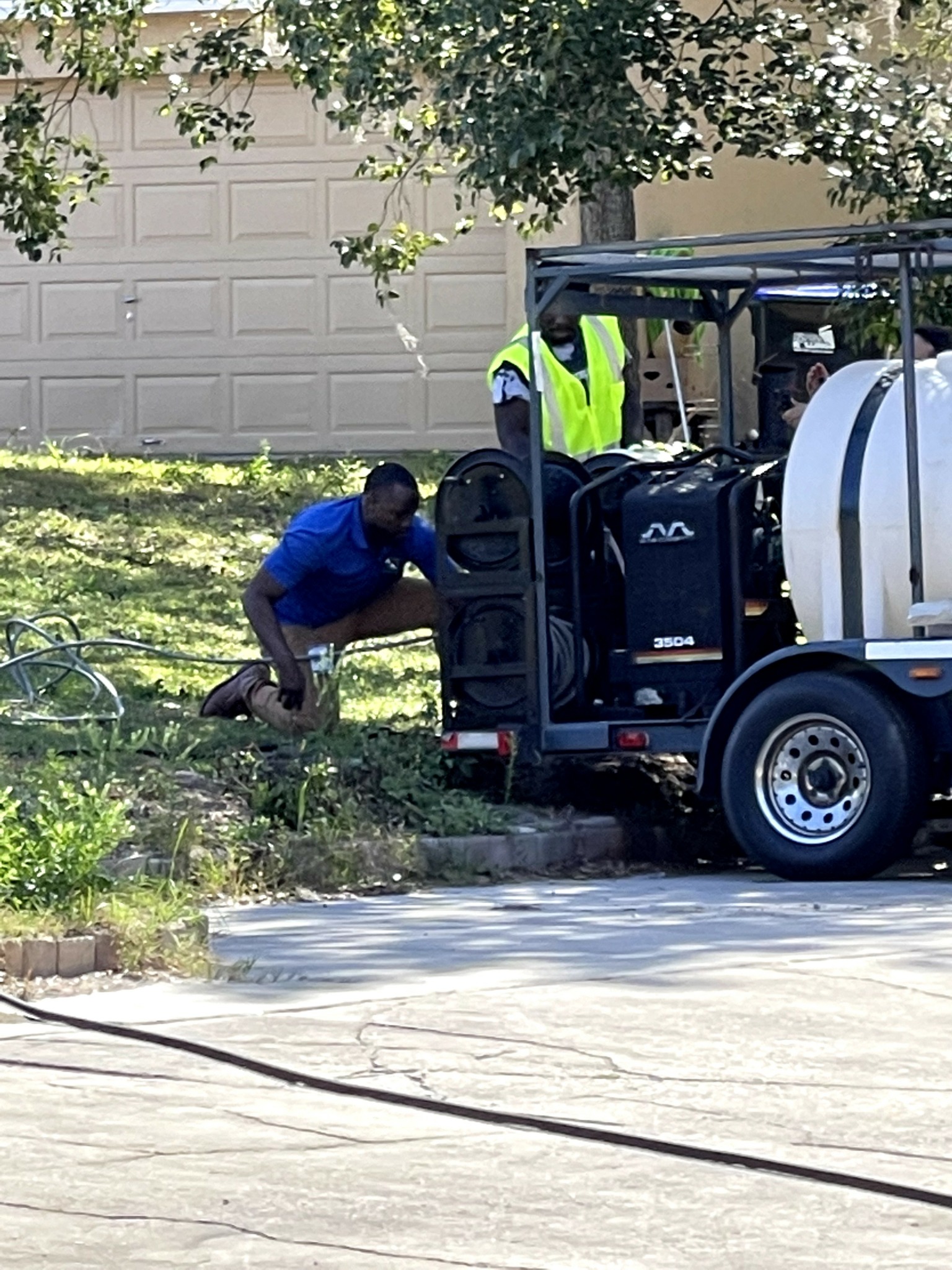 Person crouching near a utility vehicle with equipment, in front of a garage door and trees.