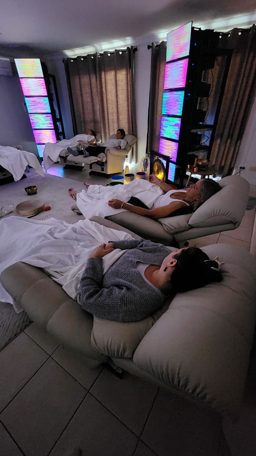 People relaxing on couches in a room with colorful LED lights and curtains, some lying down, some sitting.