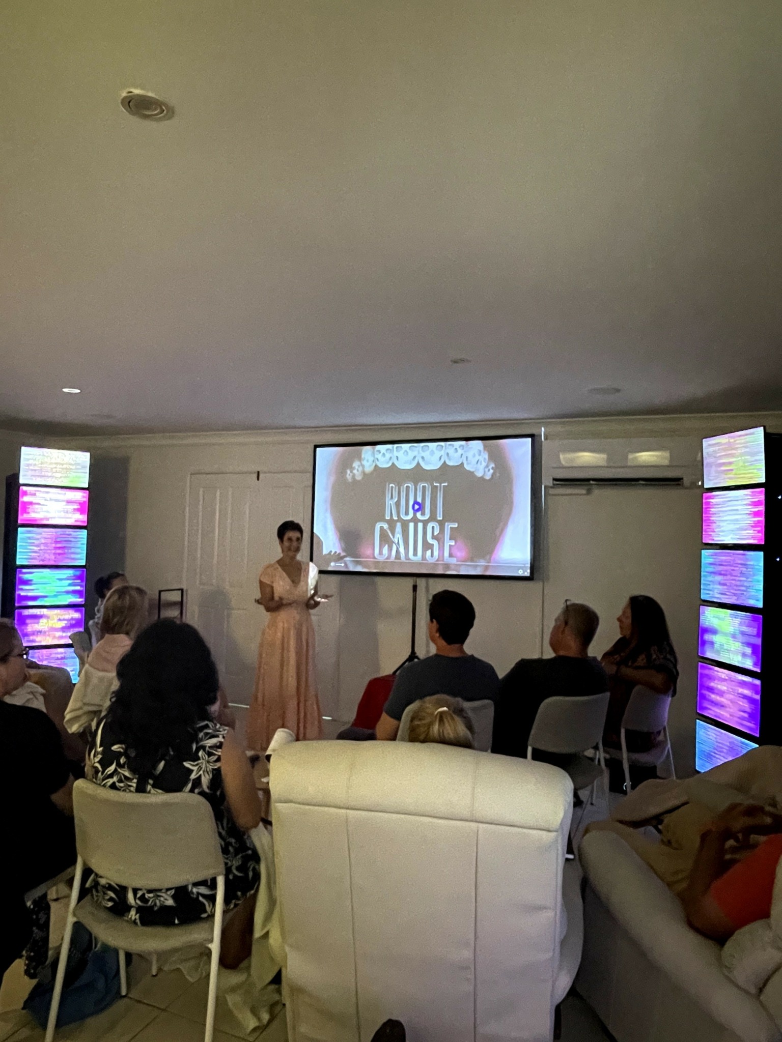 Person standing in front of a screen with a group seated facing forward, in a room with colorful side panels.