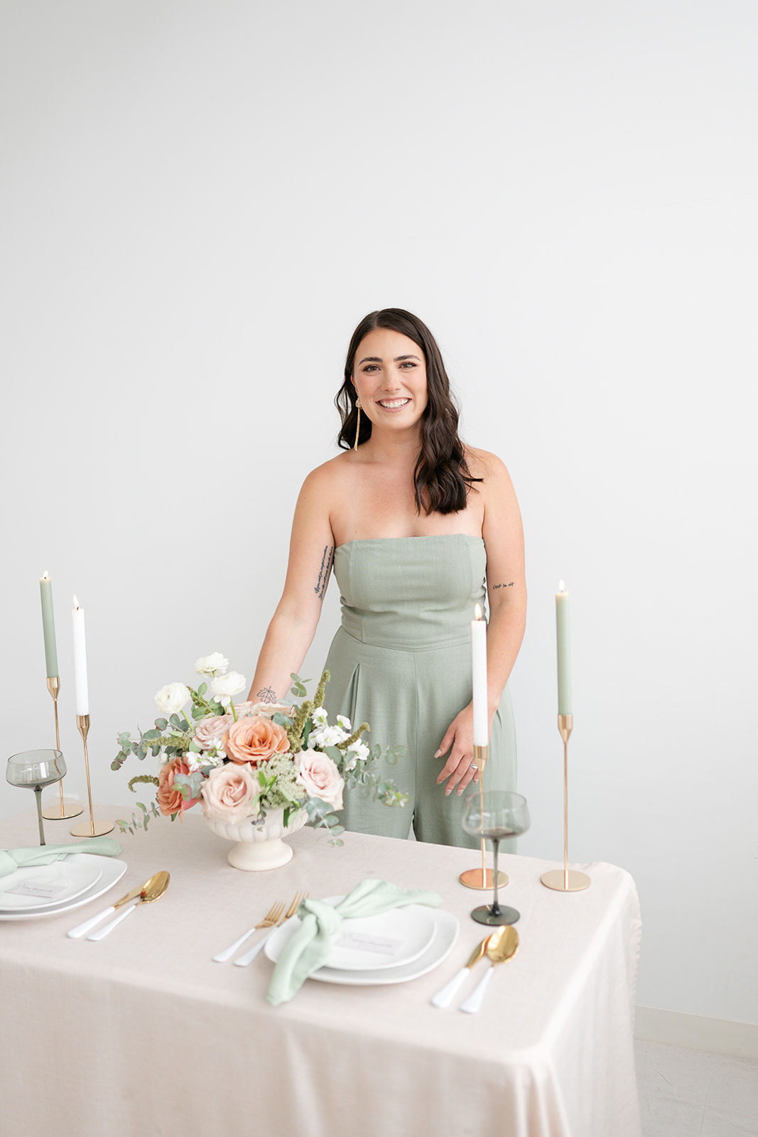 Young woman in strapless dress standing behind a decorated table with flowers and candles.