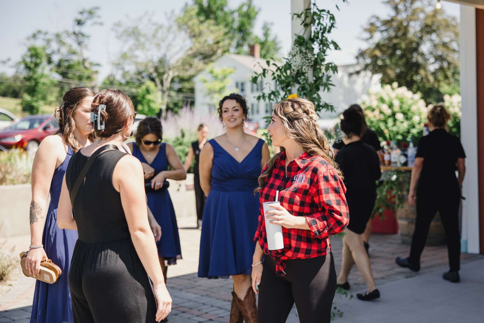 Group of women standing outdoors, talking, with trees and buildings in background.