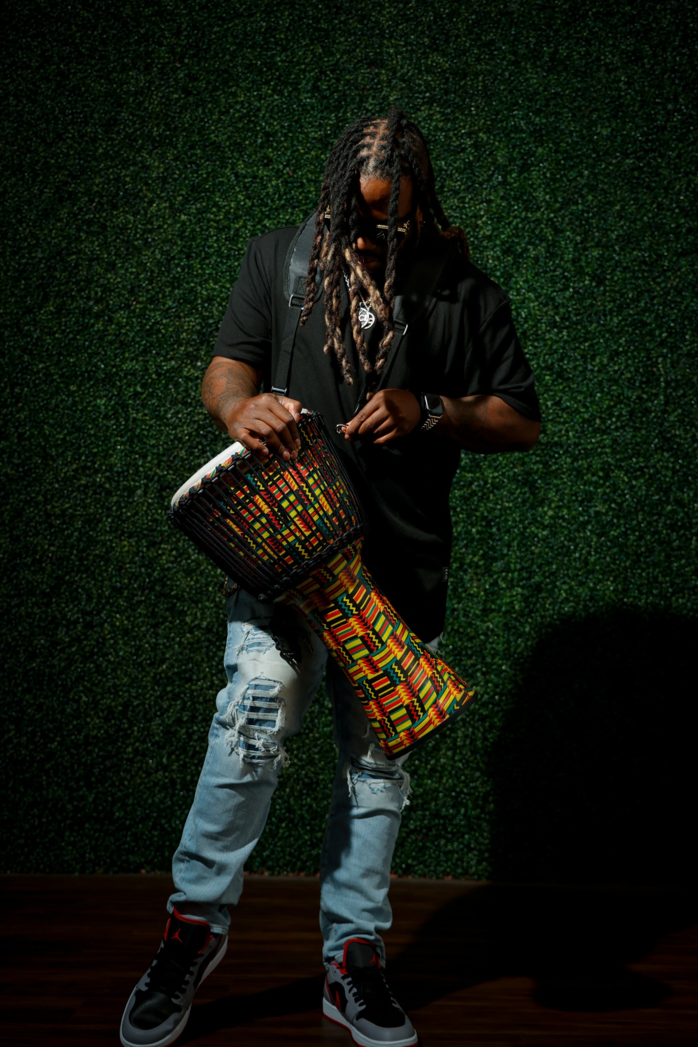Person with long hair holding a colorful drum, standing against a green textured background.