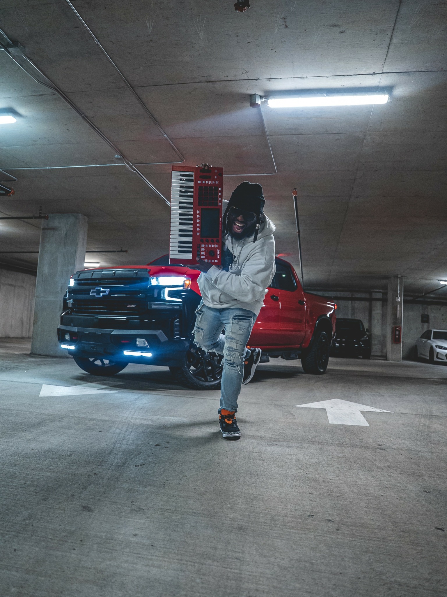 Person standing in parking garage with a red truck and a blue car behind them, overhead lights illuminating the scene.