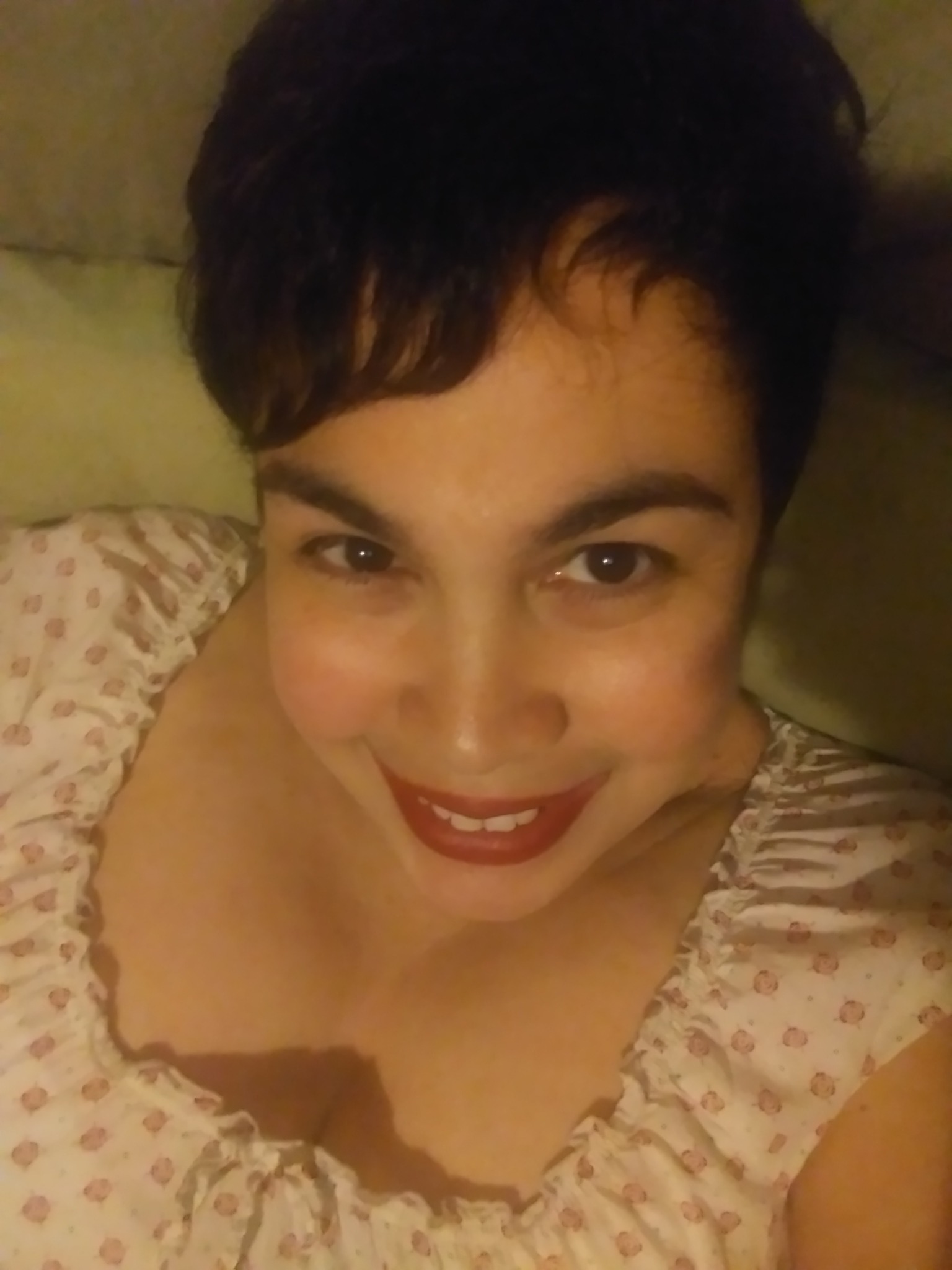 Person with short dark hair smiling, lying on a patterned pillow, wearing a light-colored top.