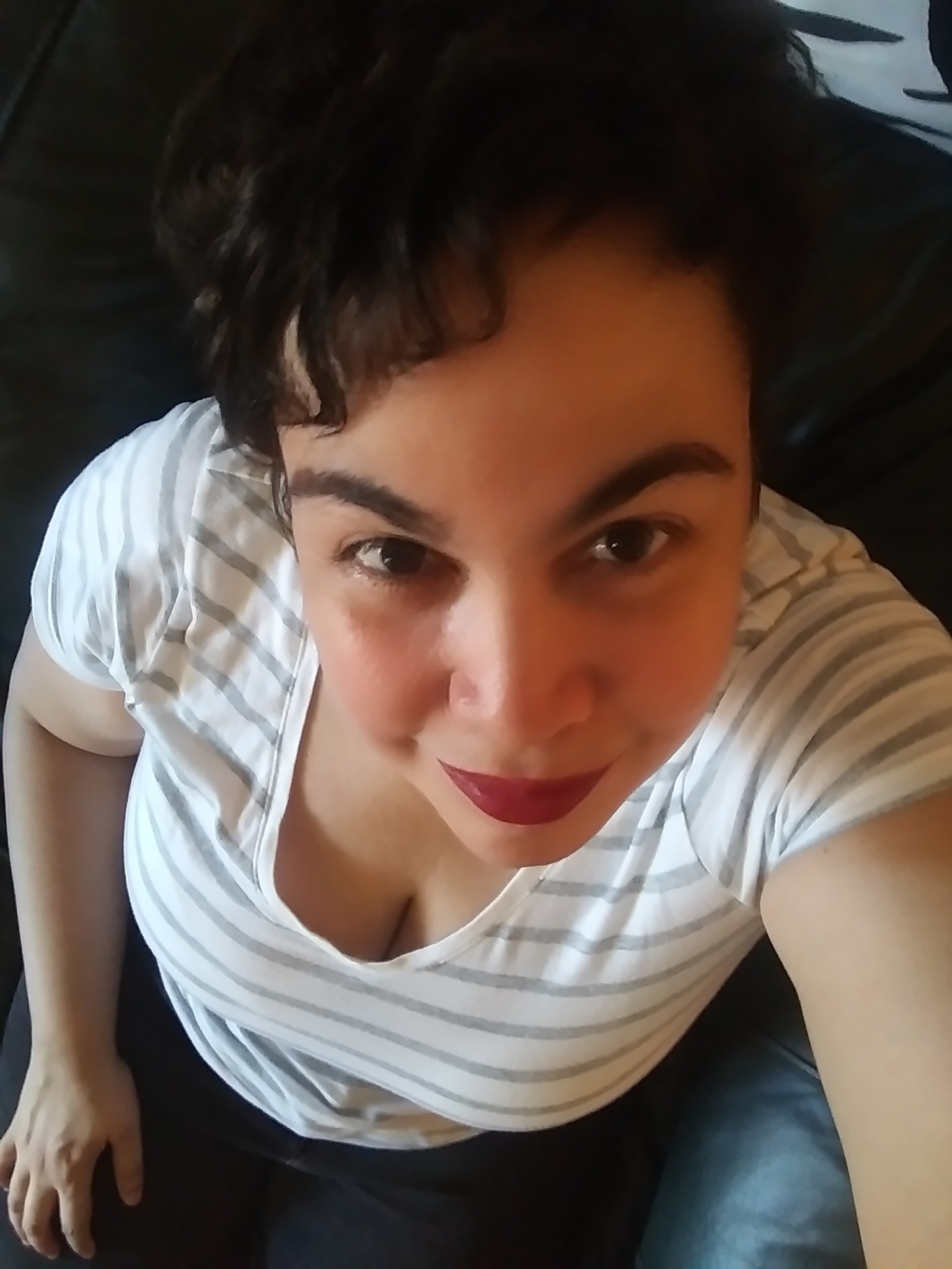 Young woman with short dark hair, wearing striped shirt, looking up at camera, smiling slightly.