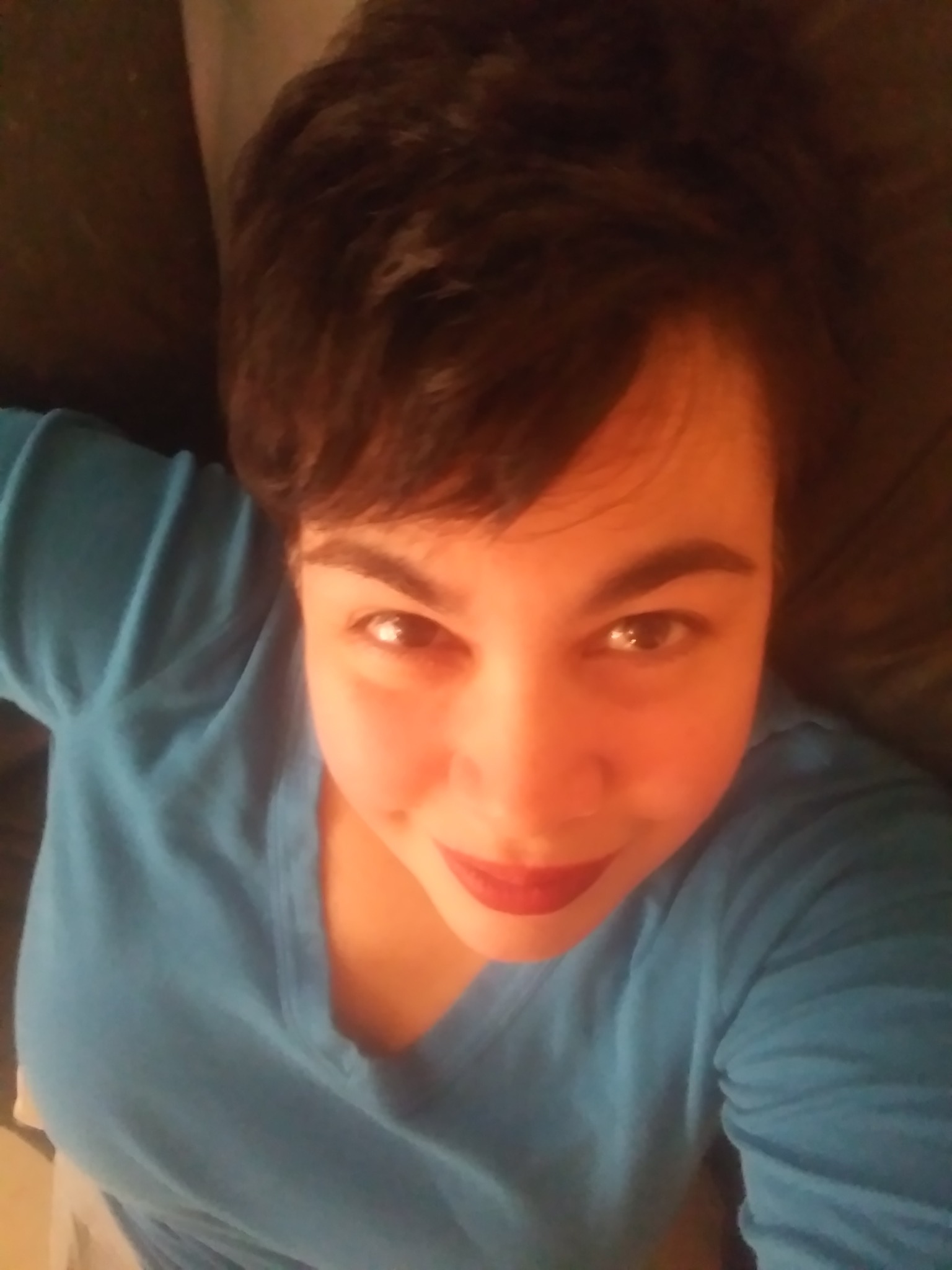 Person with short dark hair wearing a blue shirt, smiling, lying down indoors.