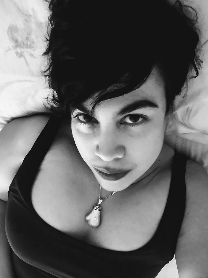 Black and white close-up of a woman lying down, wearing a black top and a necklace, with short dark hair.