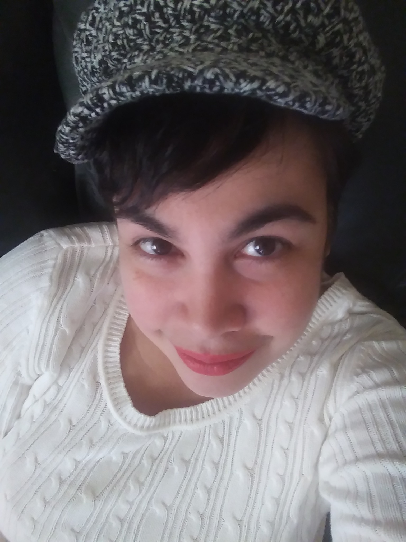 Close-up of a person wearing a patterned hat and a white textured top, looking at the camera.