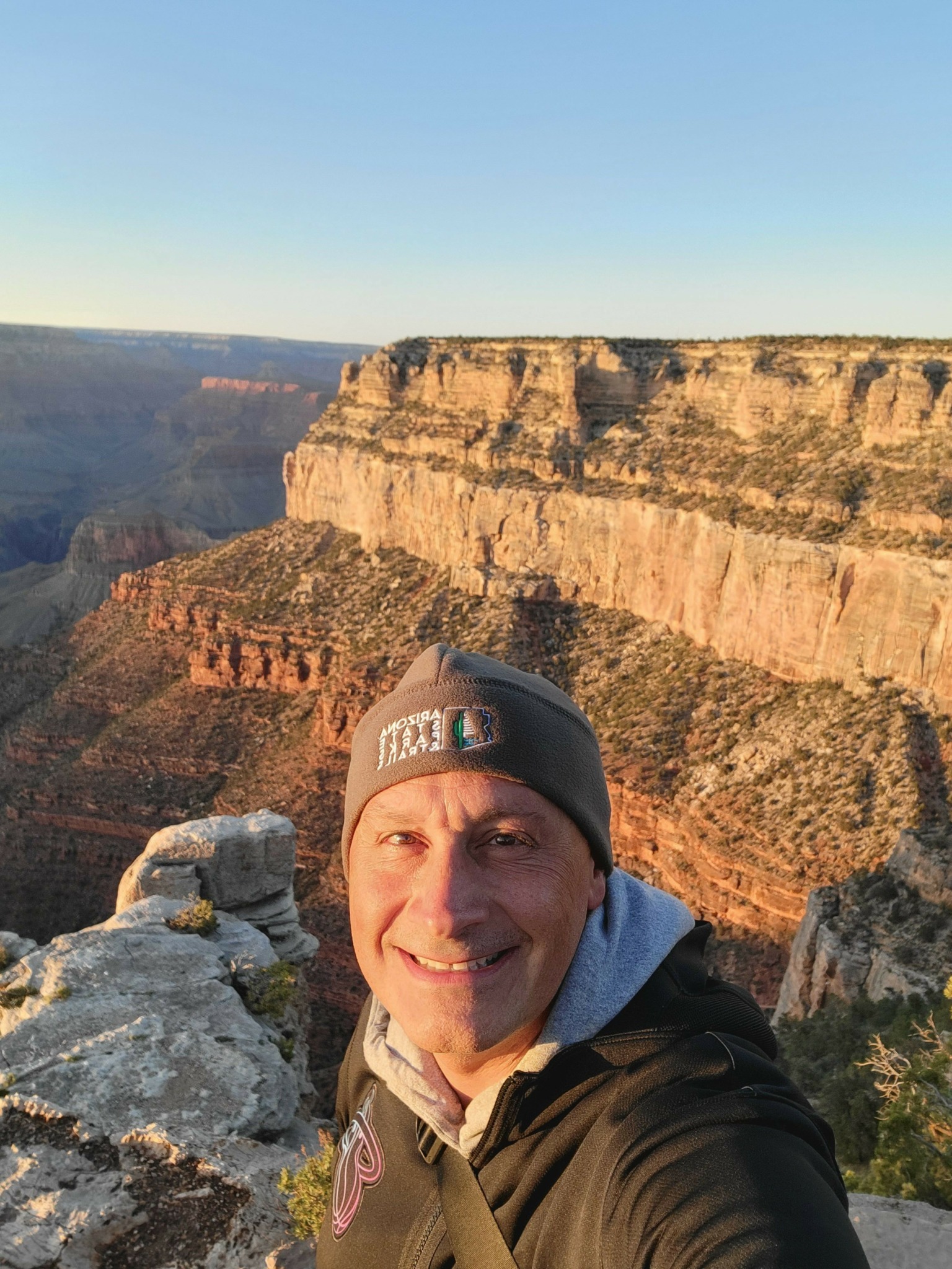 Person wearing a beanie and jacket taking a selfie with a canyon landscape in the background.