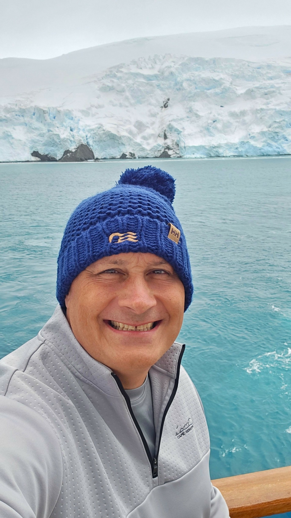 Man wearing a blue knit hat smiling in front of icy landscape and water.