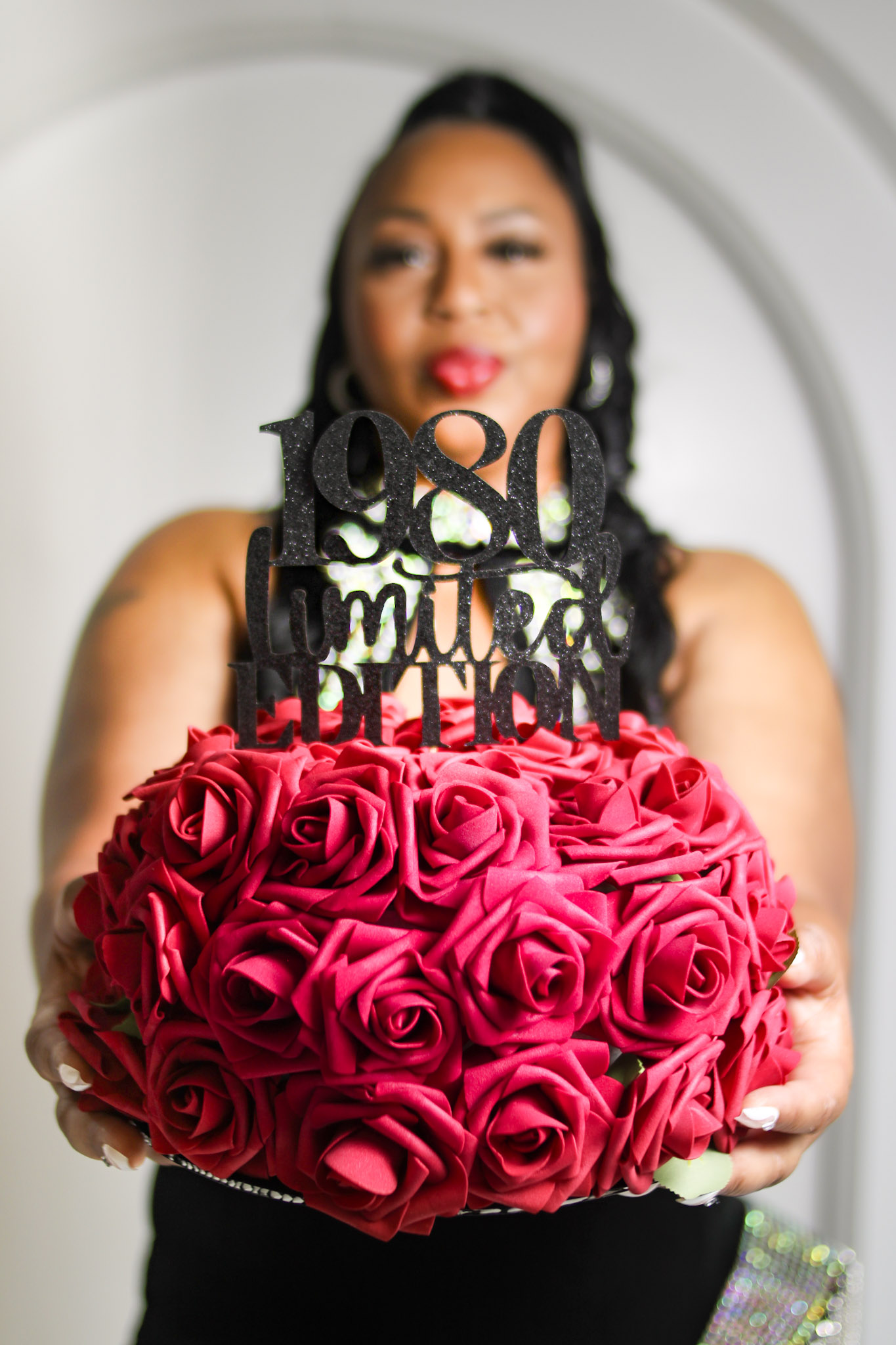 Woman holding a bouquet of pink roses with a birthday cake topper that says 'Happy Birthday 1980'.