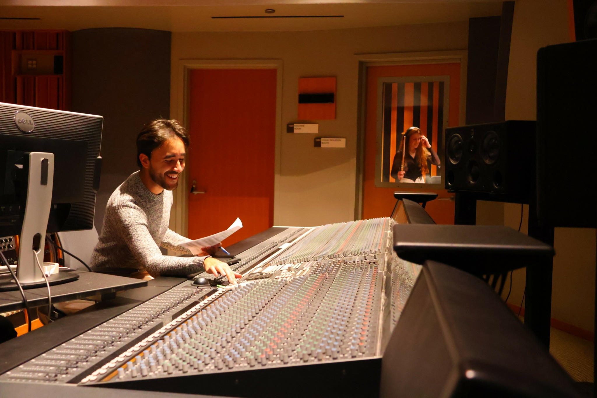 Person smiling at mixing console in recording studio with equipment and soundproofing.