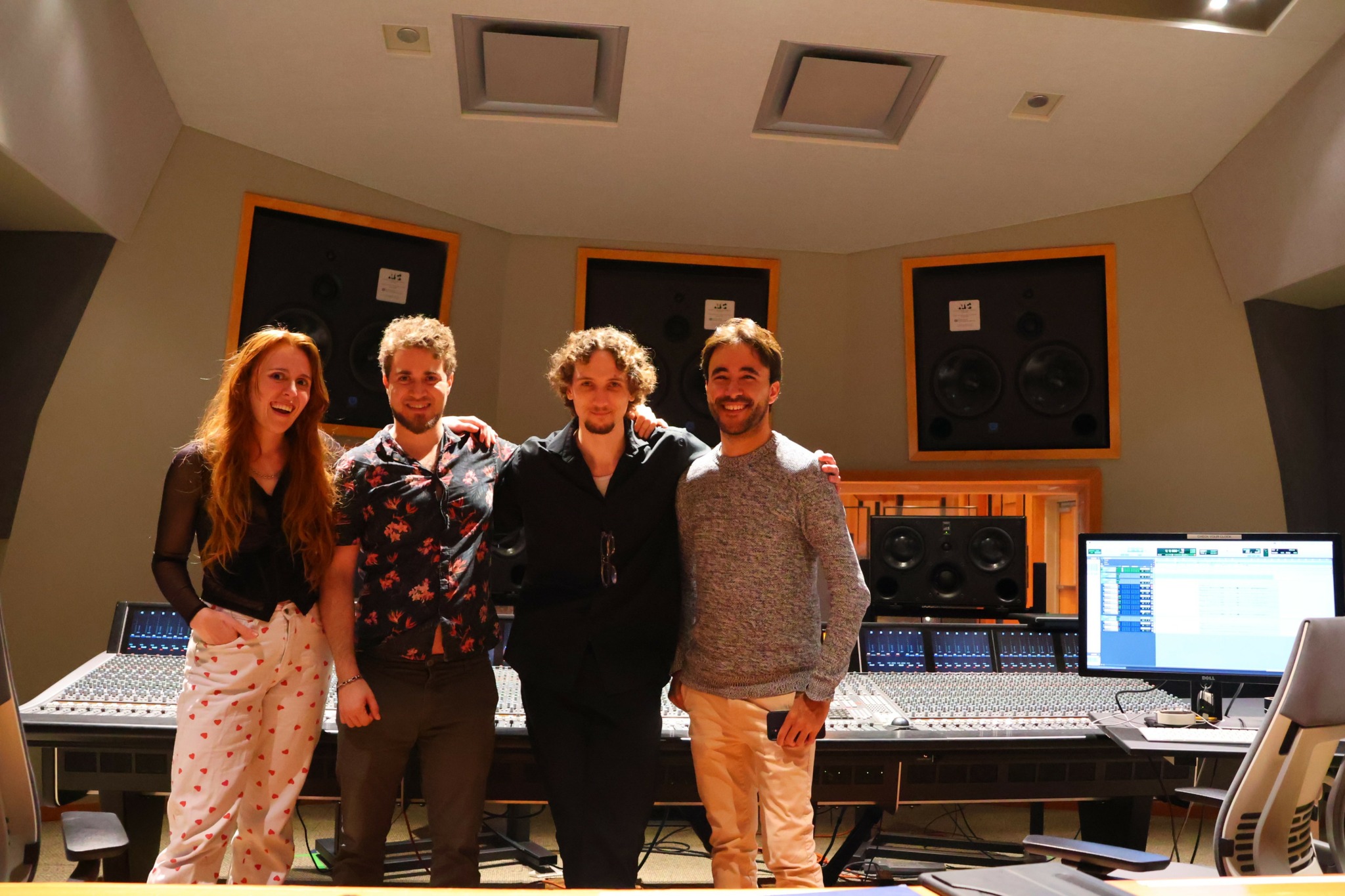 Four people standing in a recording studio with sound equipment and monitors behind them.