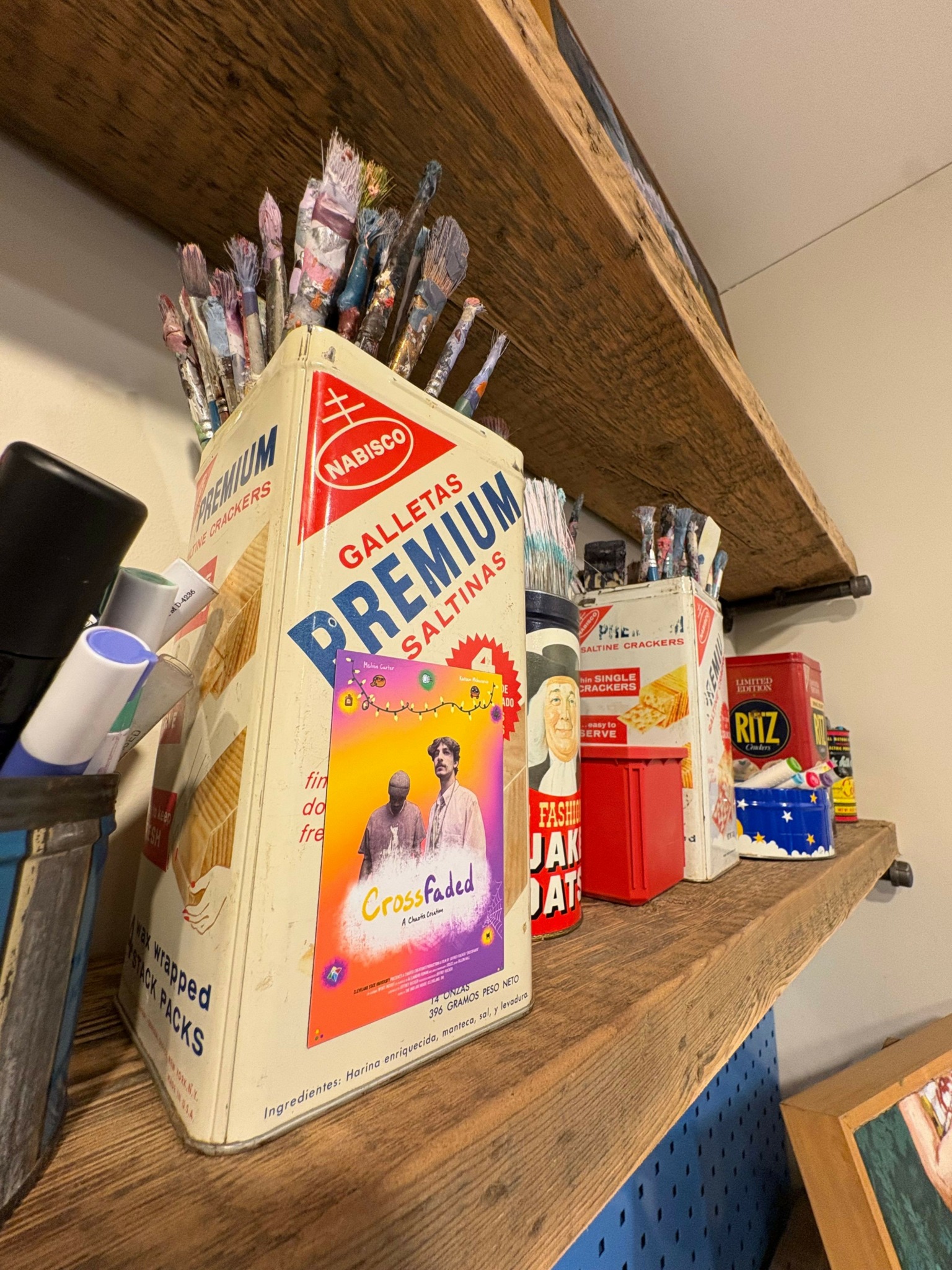 Shelf with books, pens, and small containers, with a wooden surface and a white wall background.