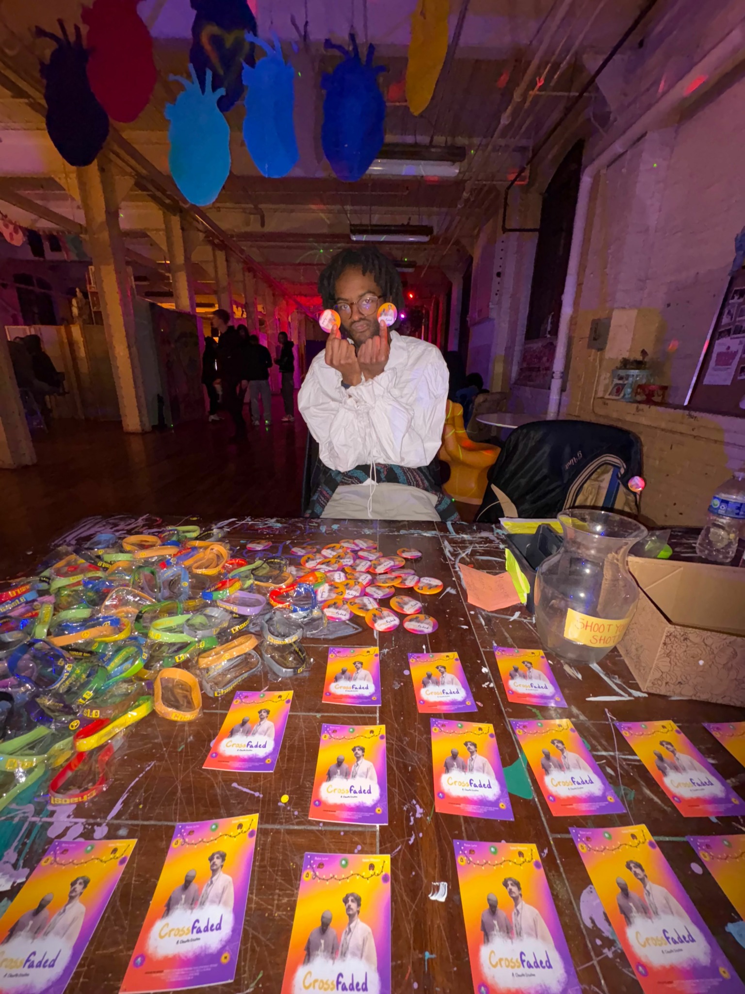 Person standing behind a table with colorful items and cards, in a decorated indoor space with hanging decorations.