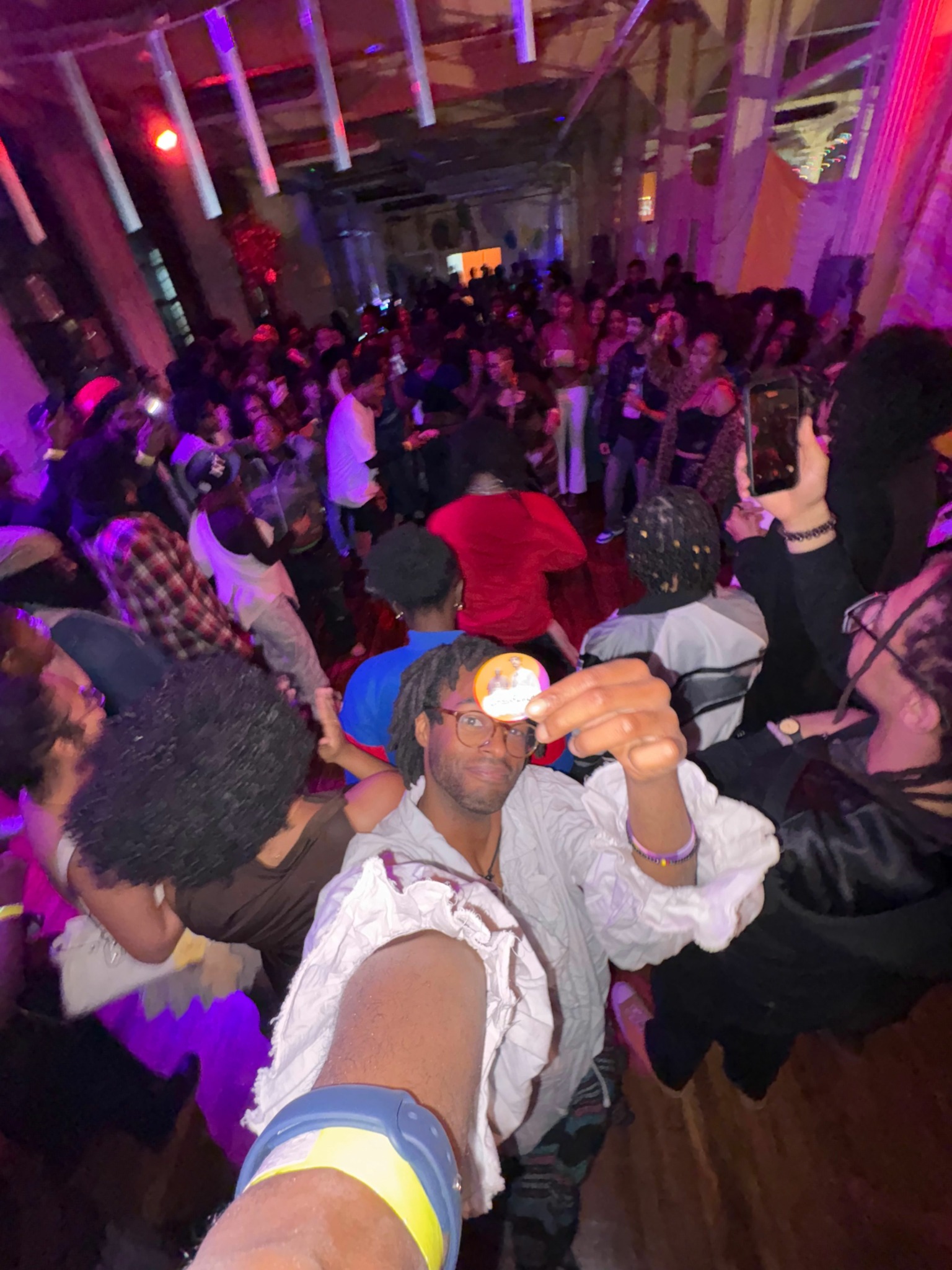 Crowd of people dancing and socializing in a dimly lit venue with colorful lighting.